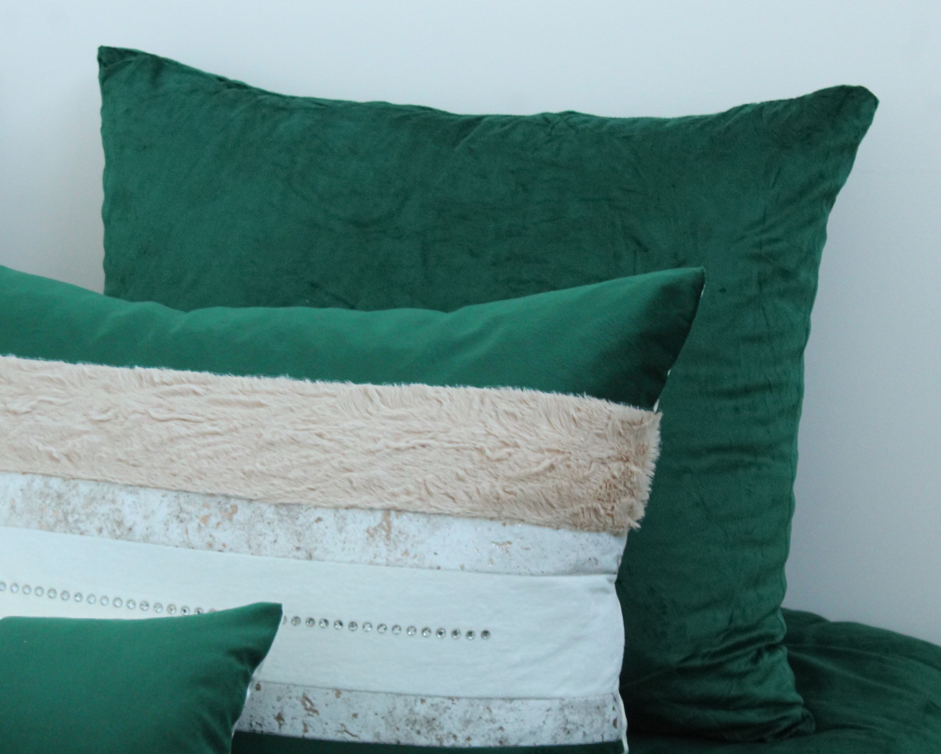 Três almofadas verdes com detalhes bege e prateados num sofá ou cama verde.