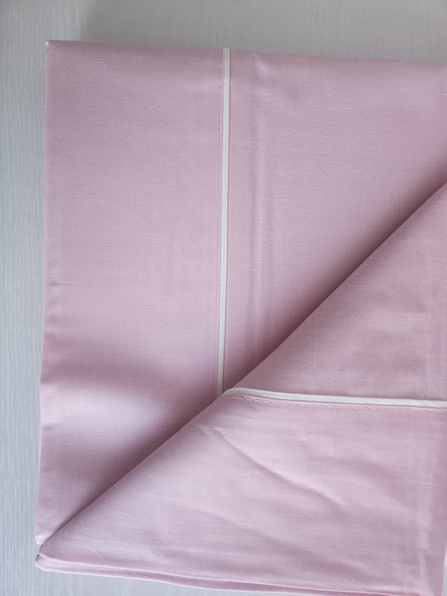 Lençol cor-de-rosa claro com costura branca dobrado sobre superfície clara