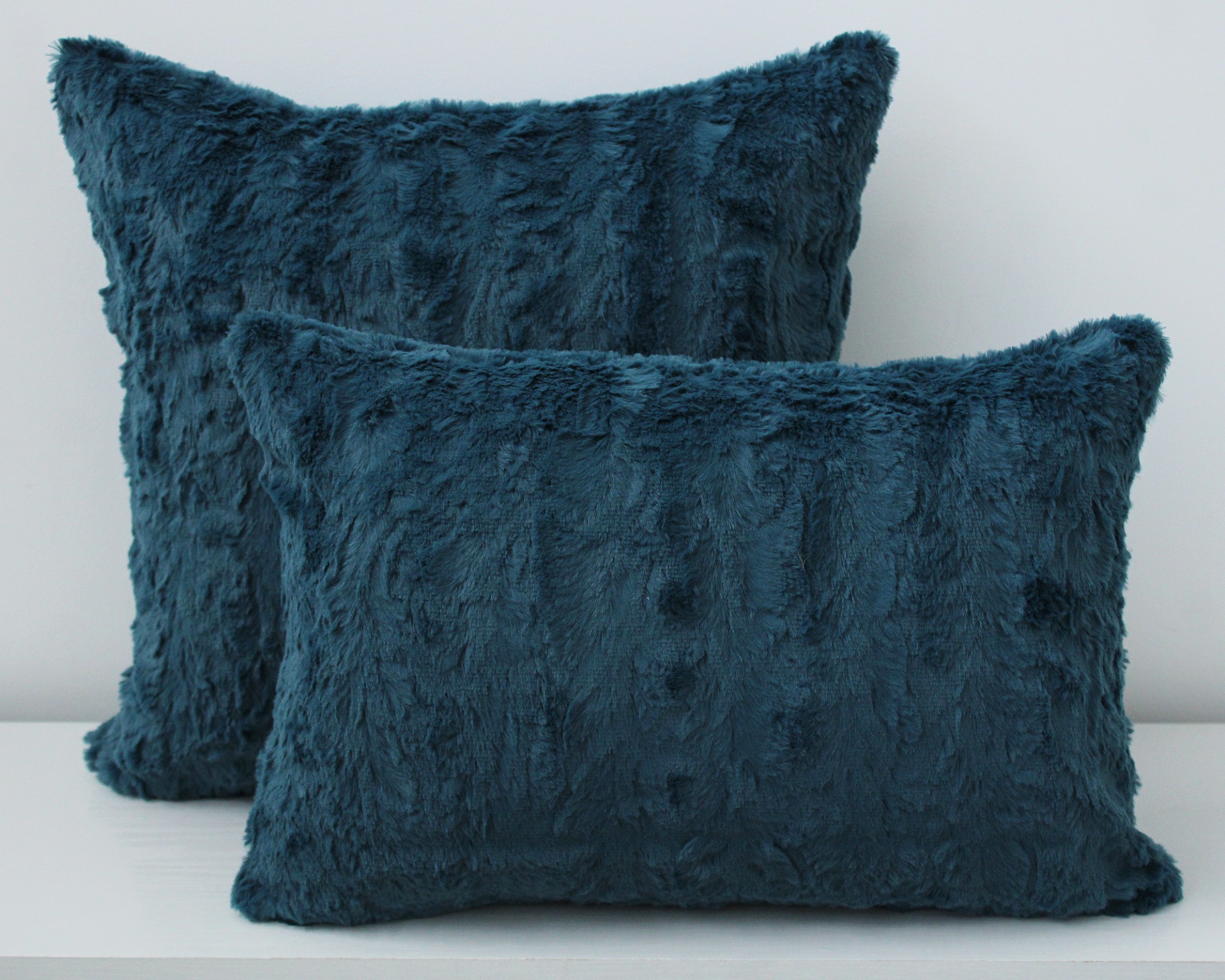 Duas almofadas felpudas azul petróleo em diferentes formatos sobre superfície branca