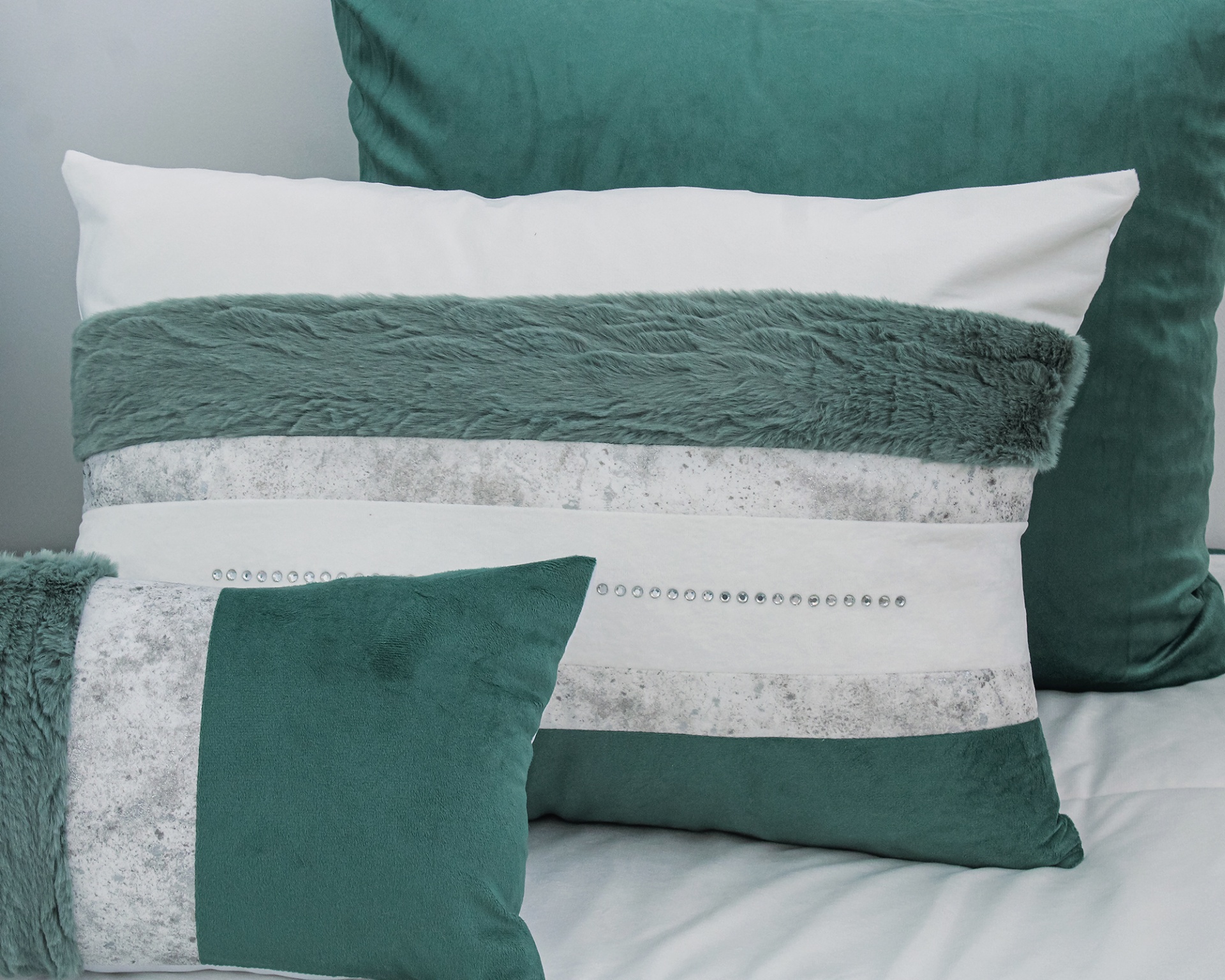 Conjunto de almofadas verdes e brancas com diferentes texturas e detalhes sobre uma cama.