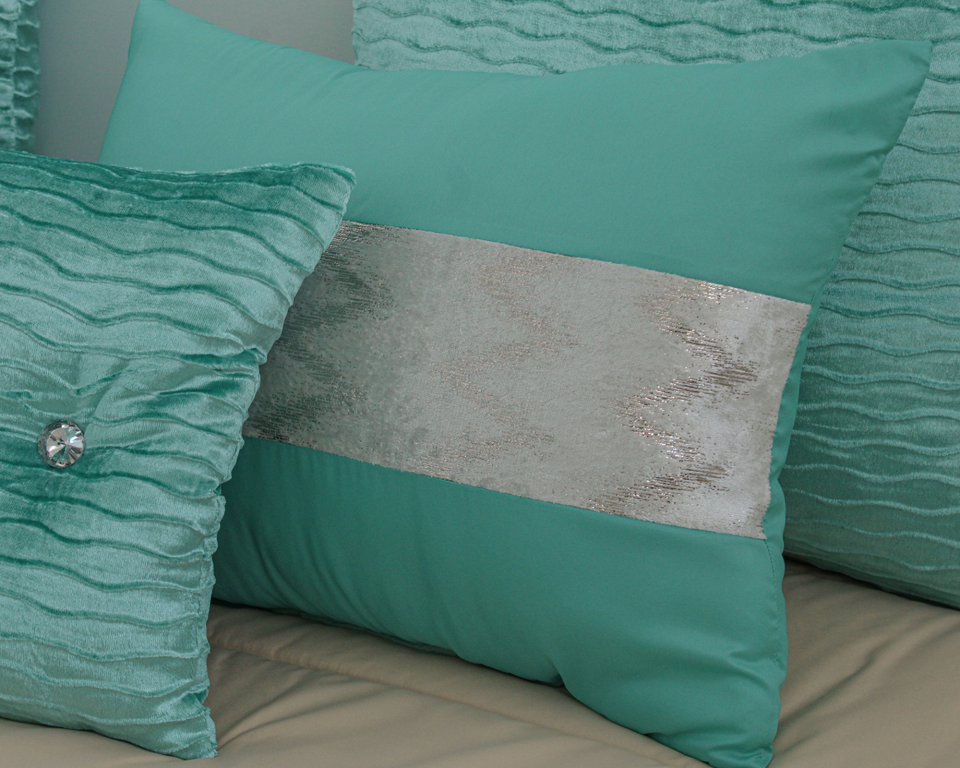 Três almofadas verdes decorativas, duas com textura ondulada e uma lisa com faixa prateada, em superfície bege