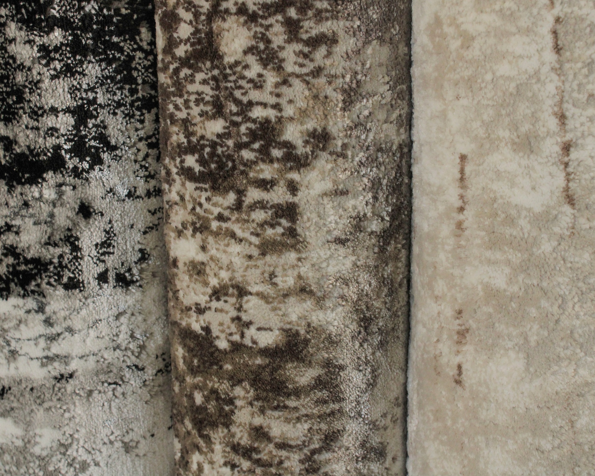 Três tapetes felpudos com padrões abstratos em tons terrosos e cinzentos.