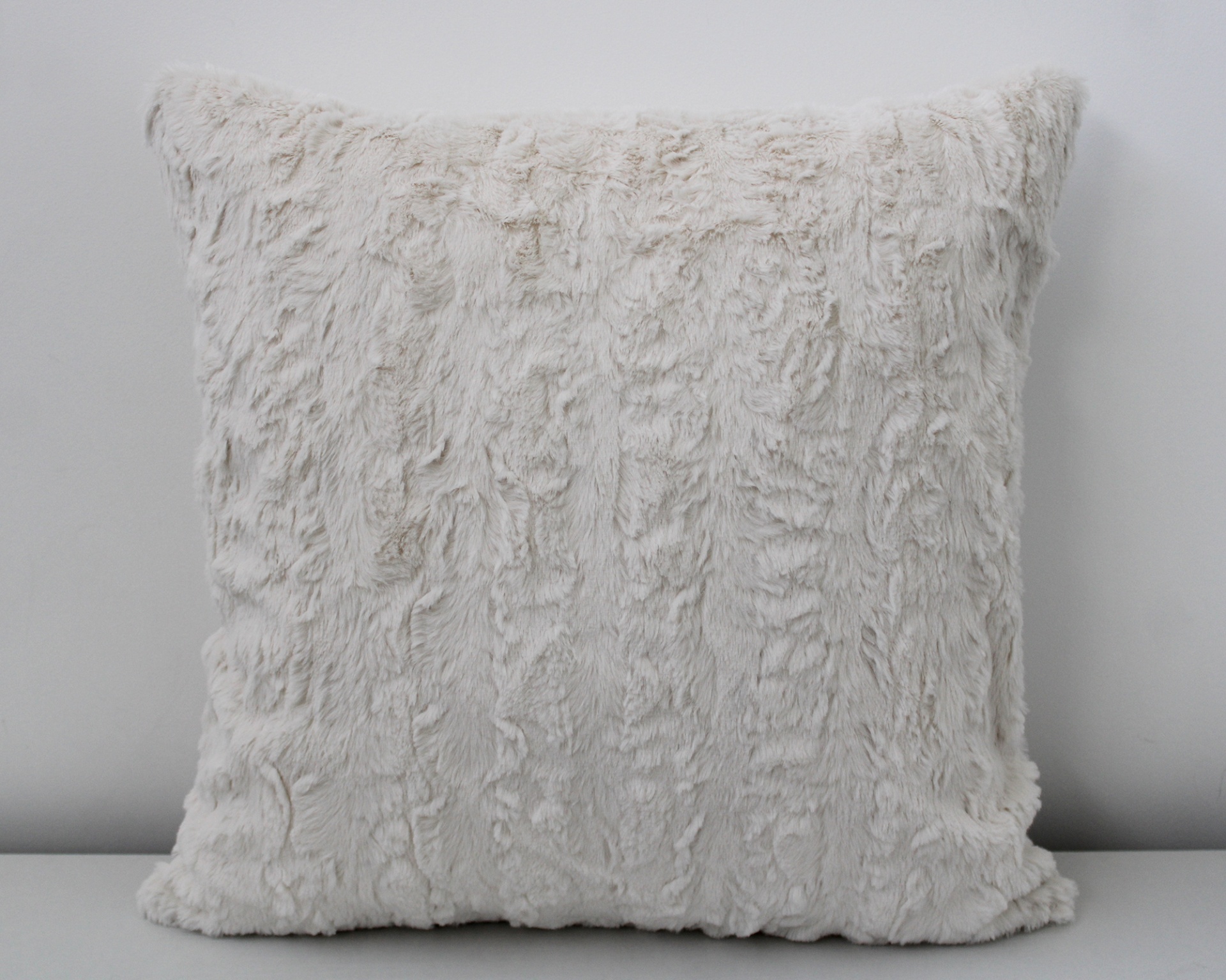 Almofada quadrada bege claro em tecido peludo contra parede branca