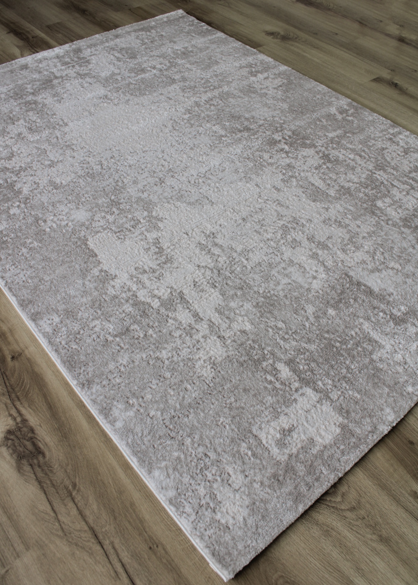 Tapete cinza-bege com padrão abstrato sobre chão de madeira clara