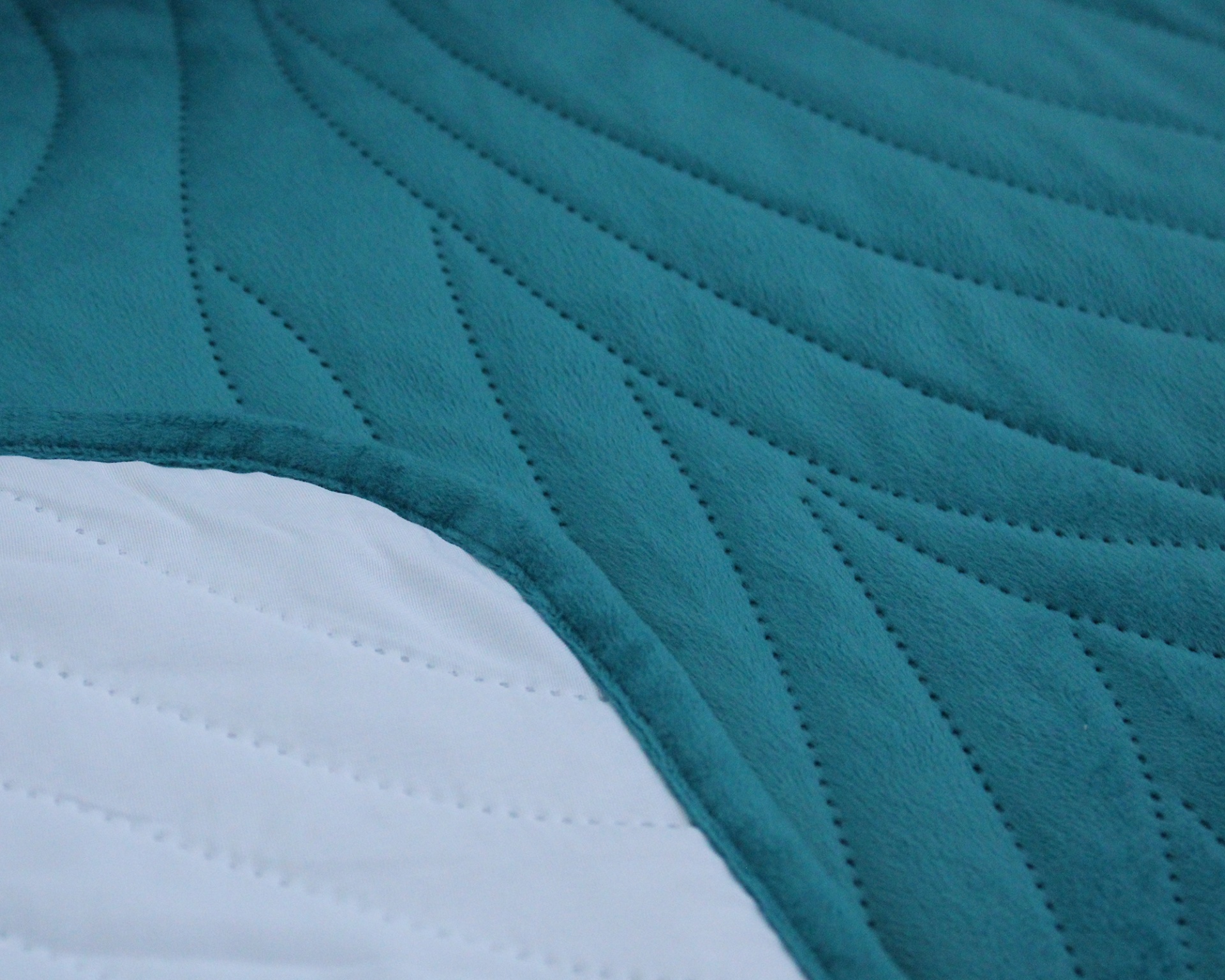 Tecidos matelassados azul turquesa e branco com padrão ondulado, sobrepostos.