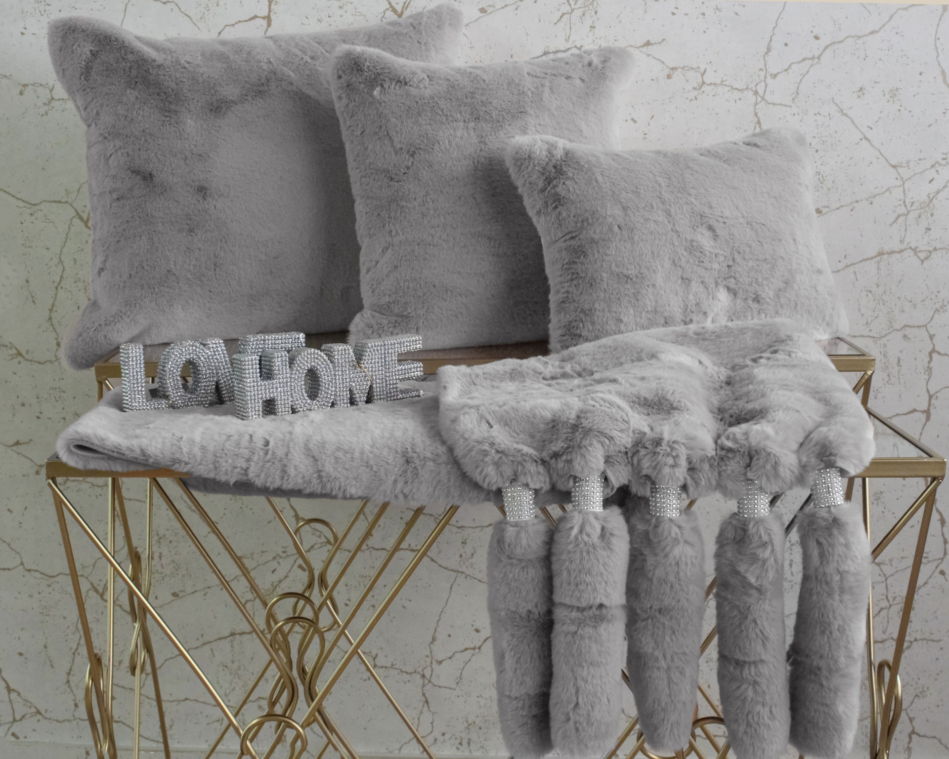Almofadas e cobertor cinza felpudo com letreiro LO HOME em superfície metálica dourada