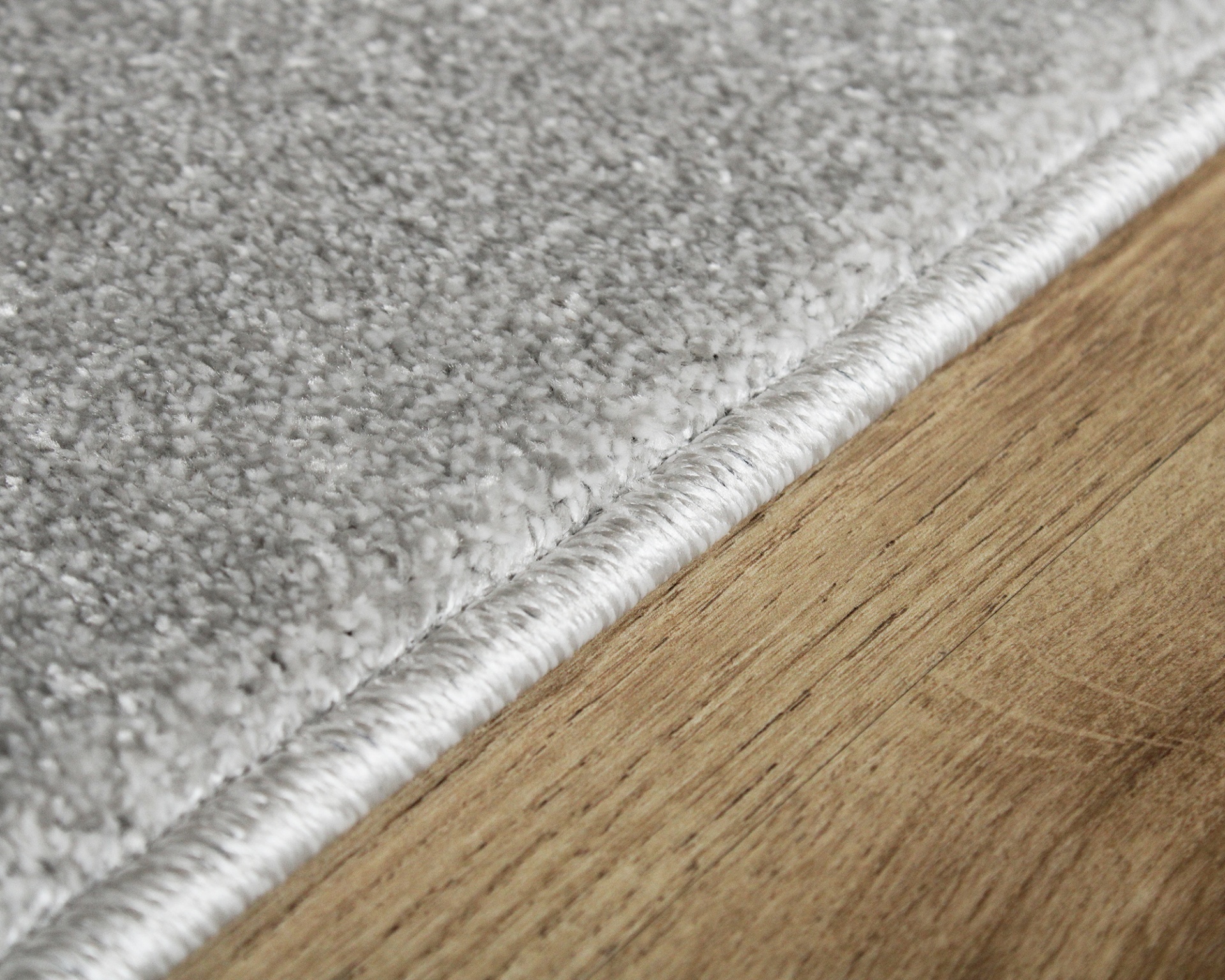 Tapete cinzento claro com borda branca sobre pavimento de madeira