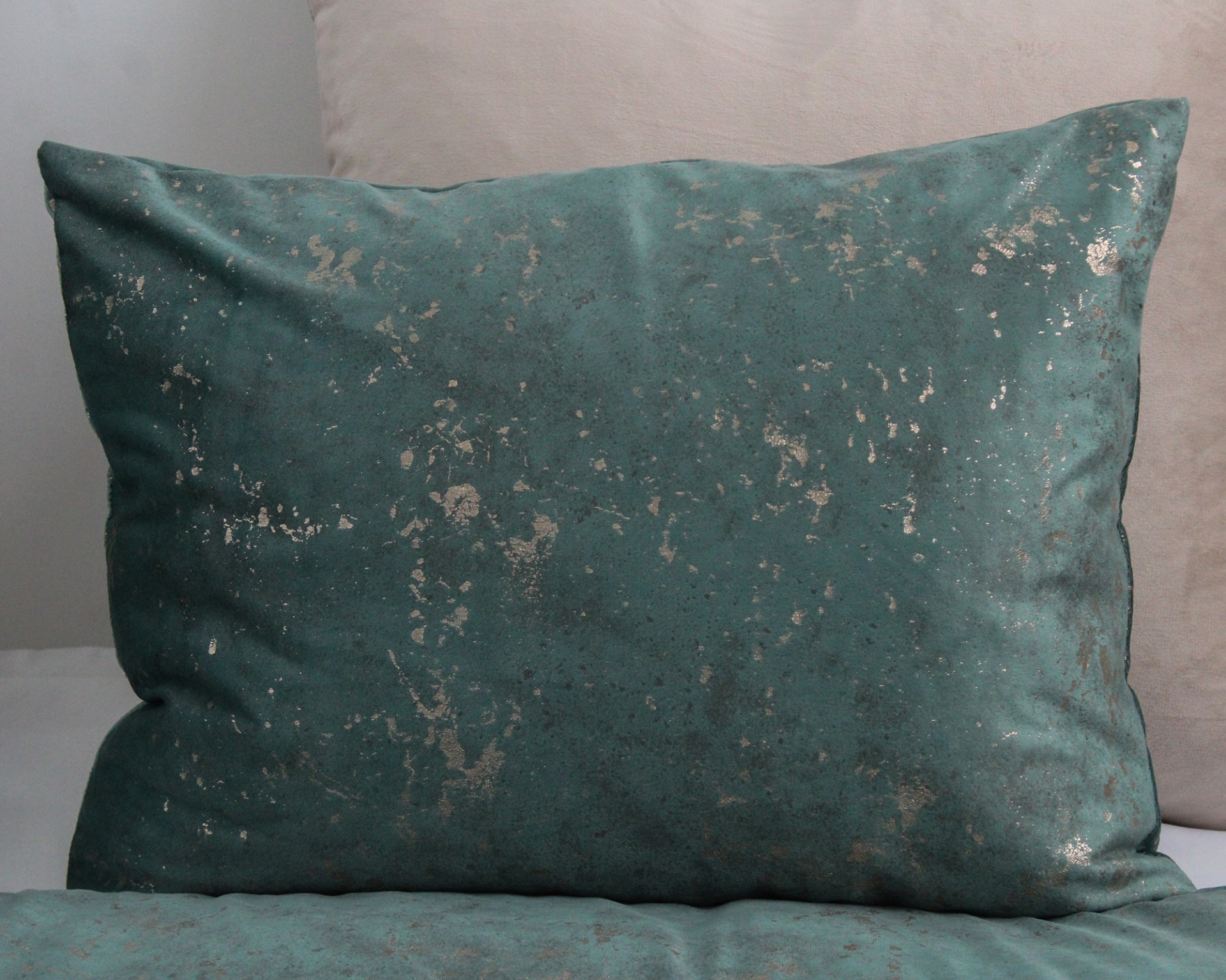 Almofada aveludada verde-azulada com manchas douradas sobre almofada bege