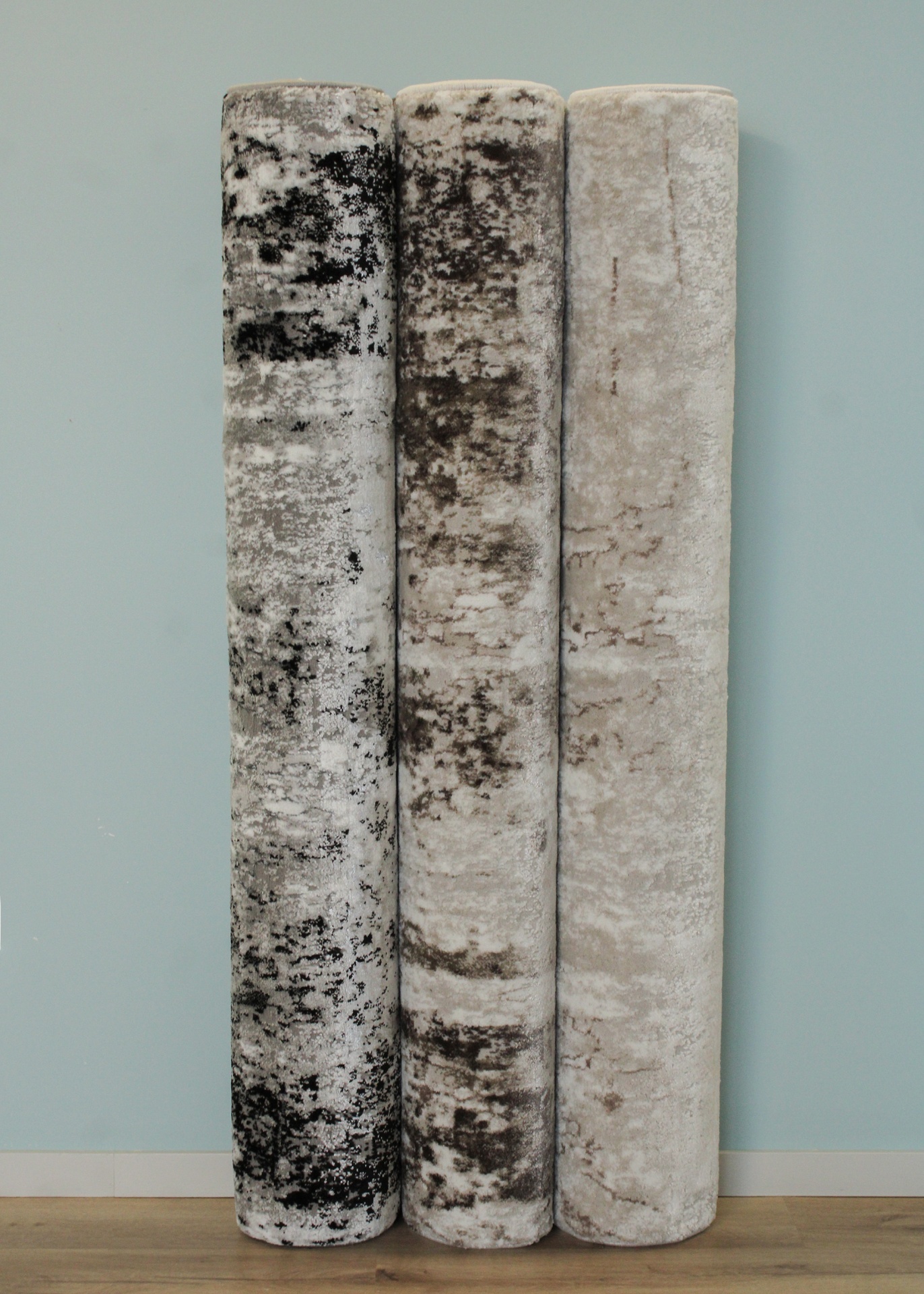 Três rolos de tapetes com padrões abstratos em tons de cinza, preto e bege