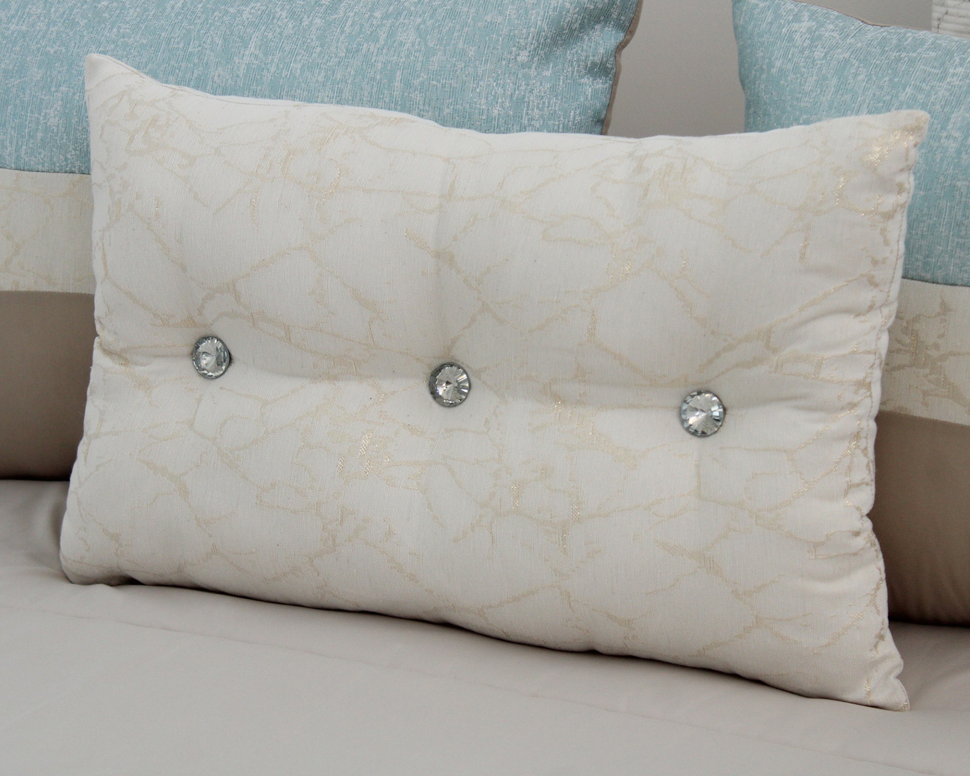 Almofada retangular branca decorativa com botões de cristal sobre cama com outras almofadas