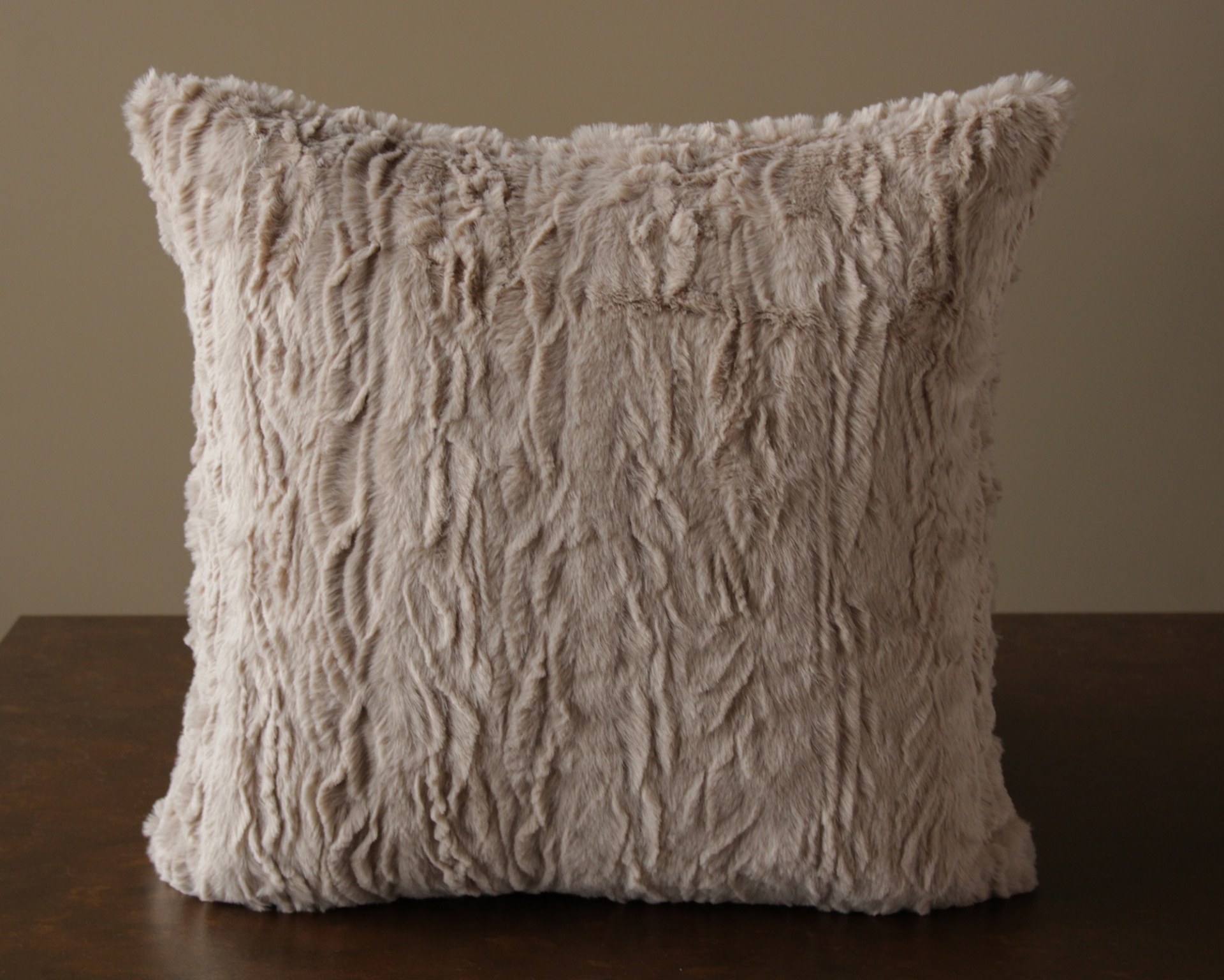 Almofada quadrada de pelúcia bege texturizada sobre mesa de madeira escura