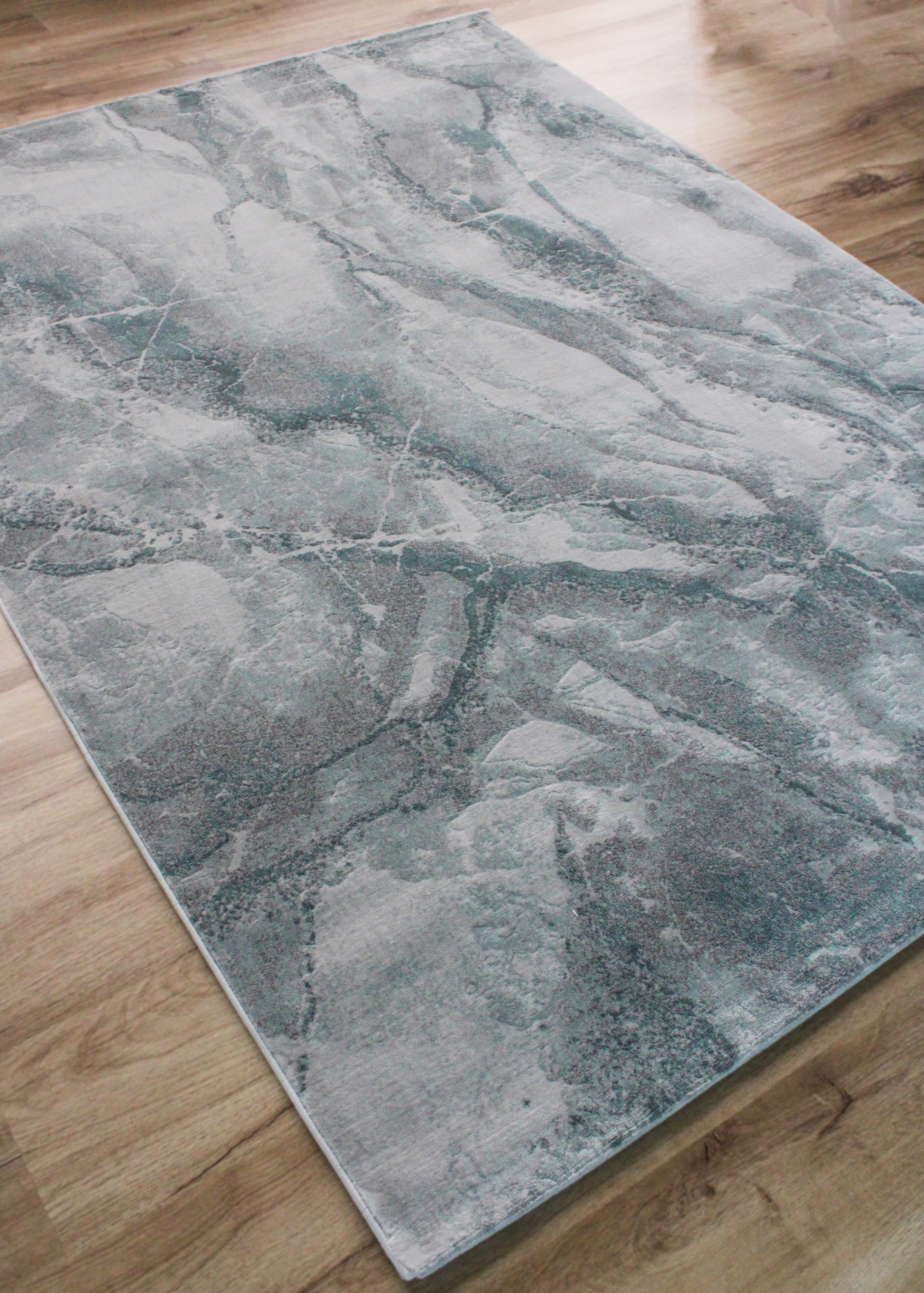 Tapete retangular com padrão abstrato cinza e azul sobre chão de madeira clara