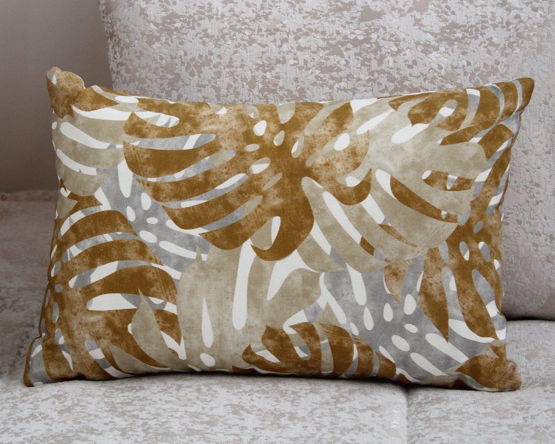 Almofada retangular com padrão de folhas castanho, bege e cinza sobre tecido branco