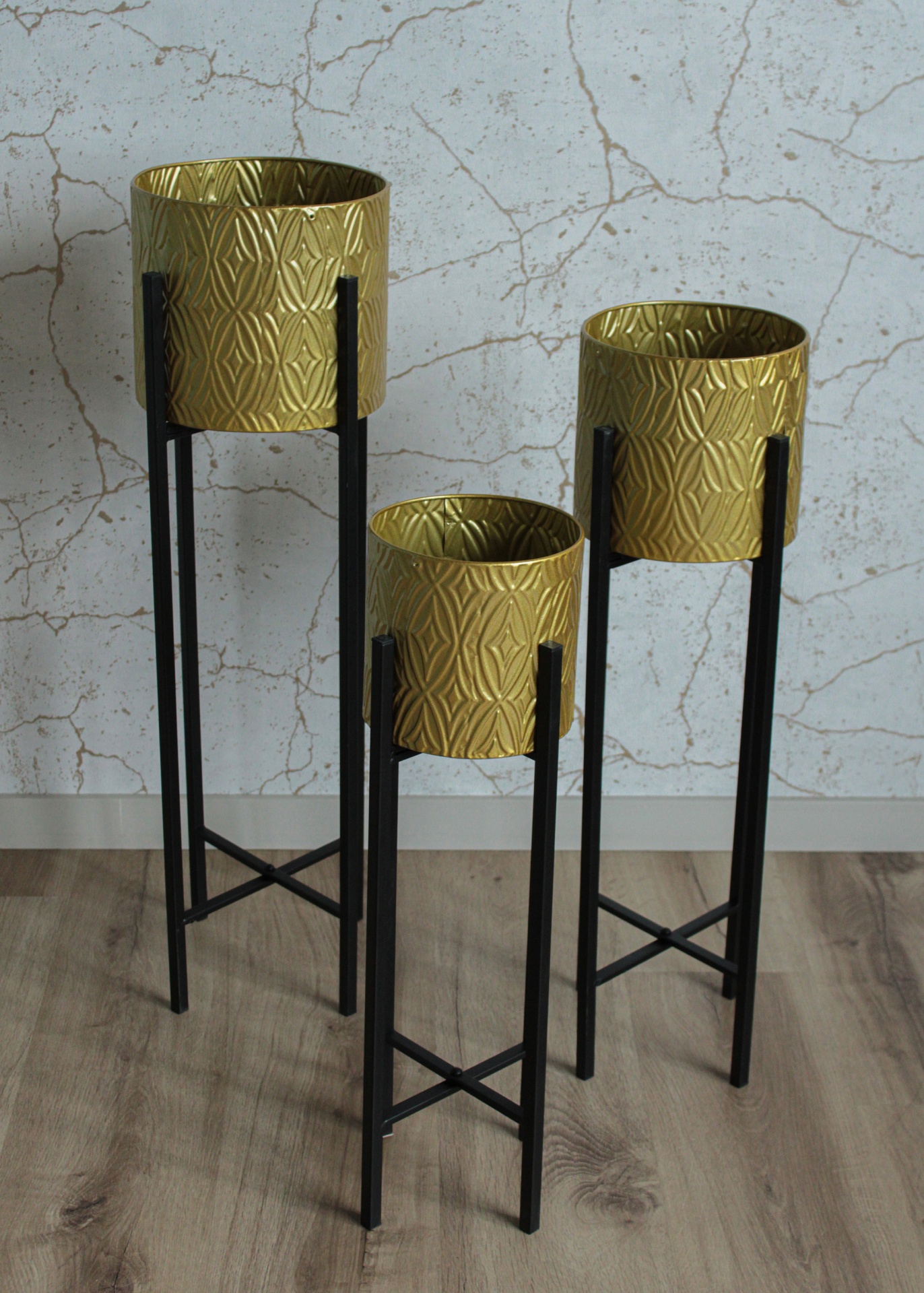Três floreiras douradas decorativas em suportes metálicos pretos