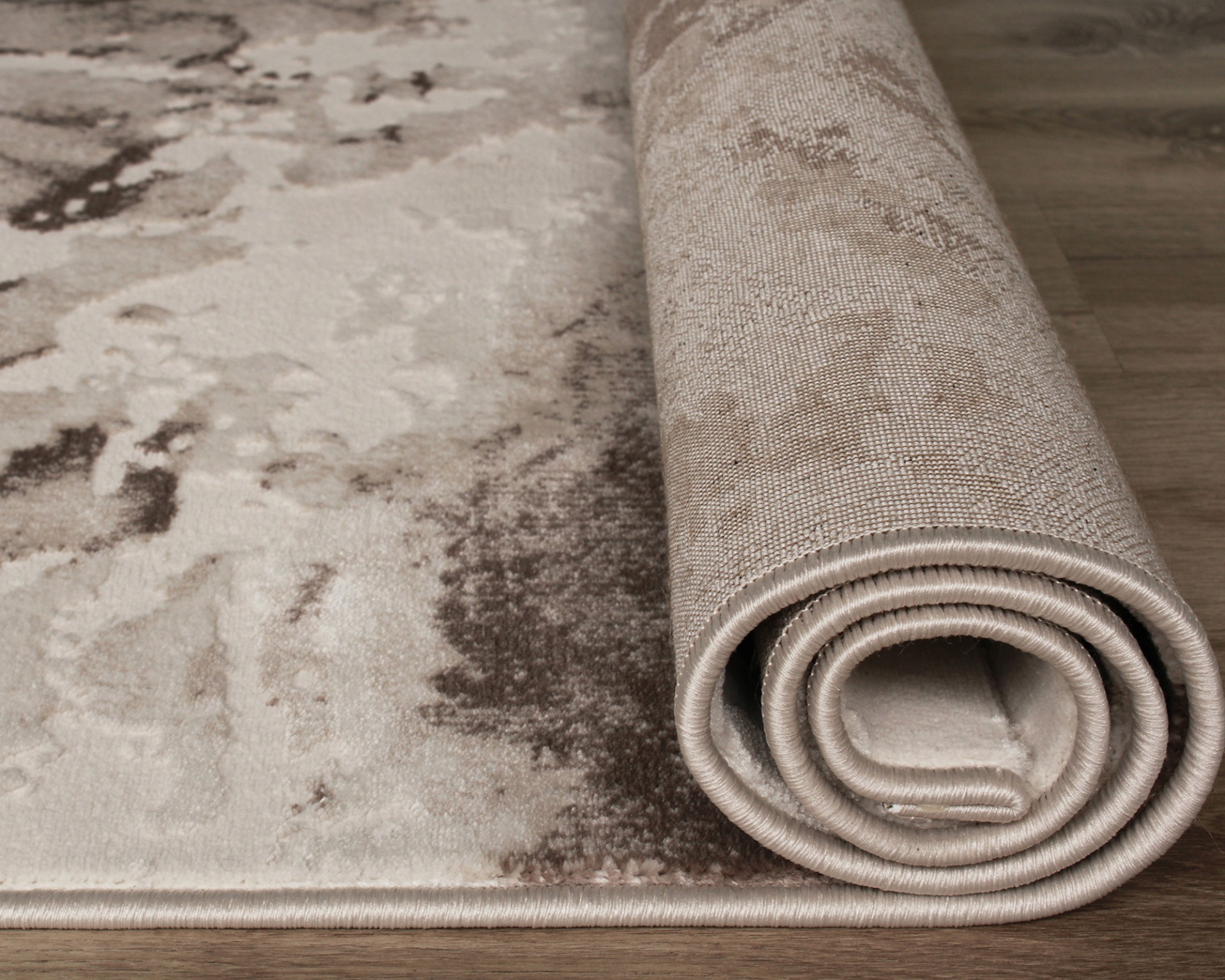 Tapete enrolado com padrão abstrato bege e castanho sobre chão de madeira.