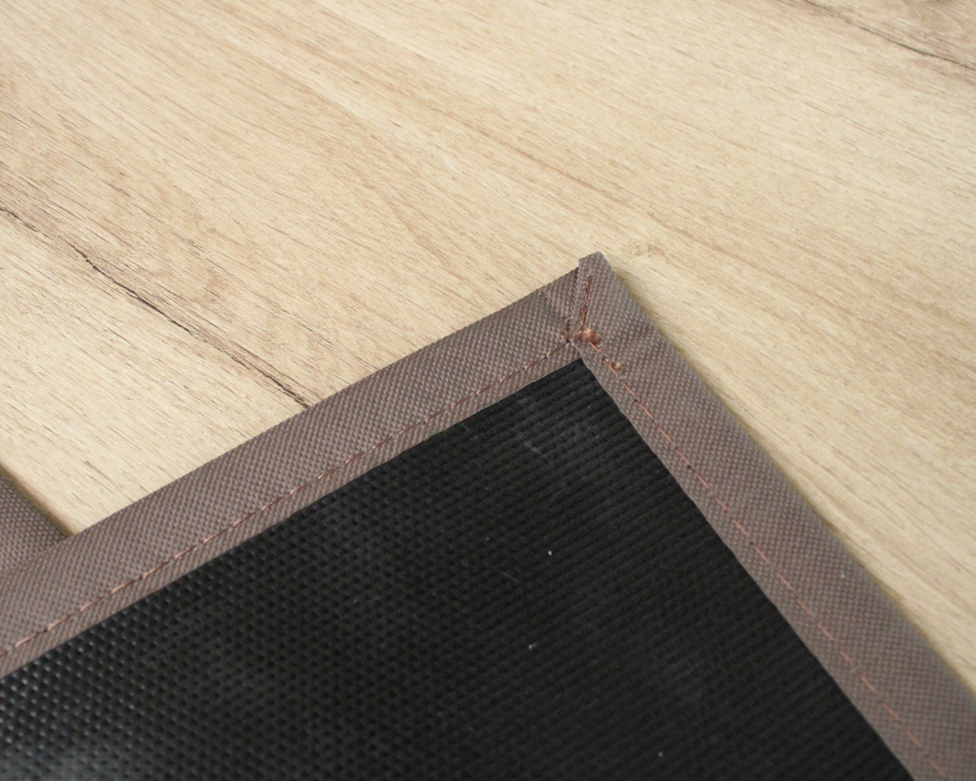 Canto de tecido preto com borda castanha sobre madeira clara