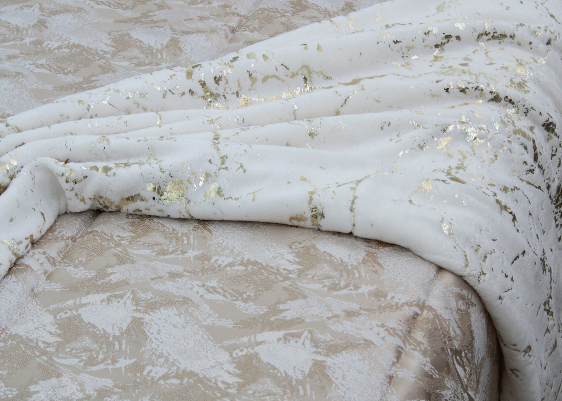 Tecido decorativo branco com detalhes dourados sobre superfície bege com padrão abstrato