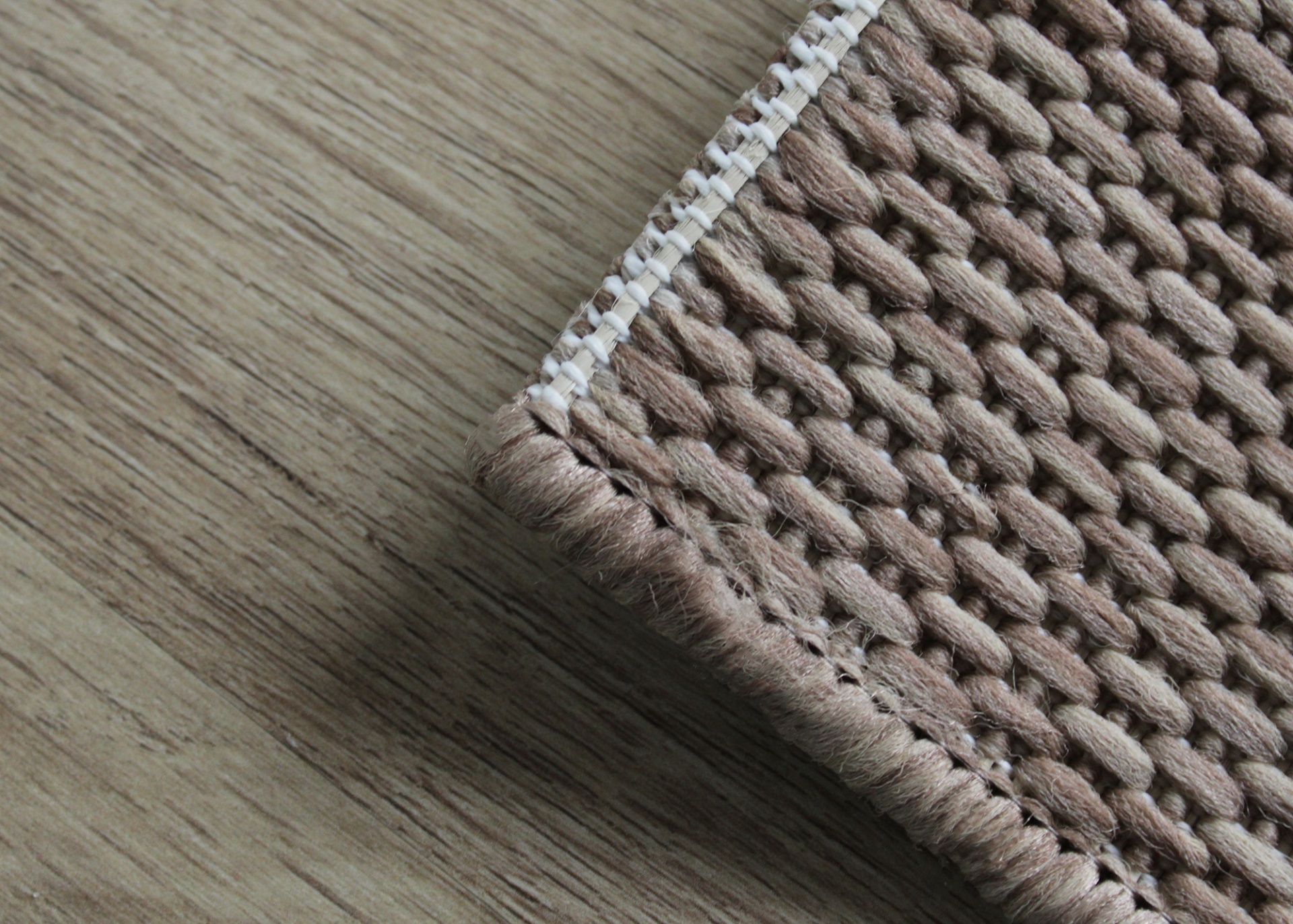 Detalhe de tapete castanho claro e bege com borda branca sobre chão de madeira clara