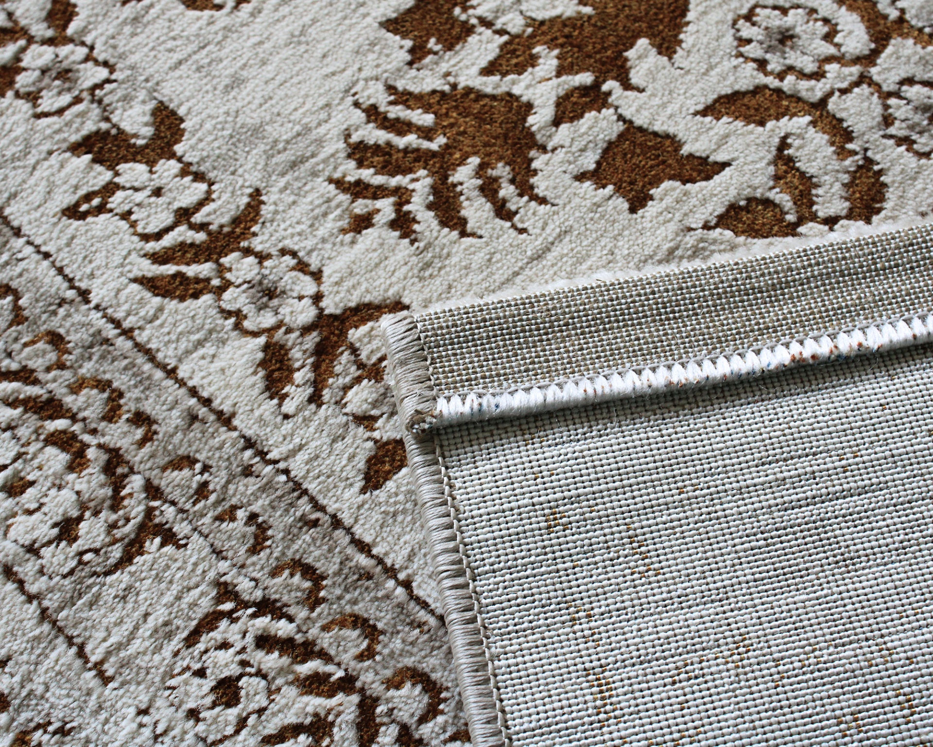 Tapete com padrão floral castanho e bege, parte de trás em tecido bege com costura reforçada.