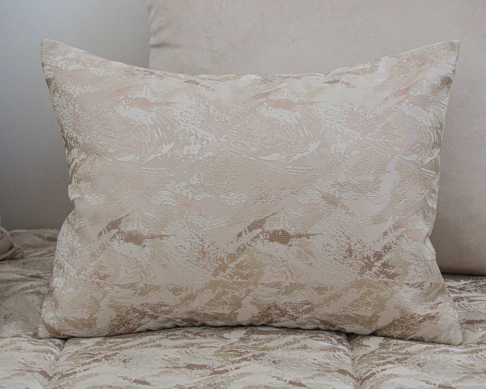 Almofada retangular bege com padrão texturizado sobre superfície macia.