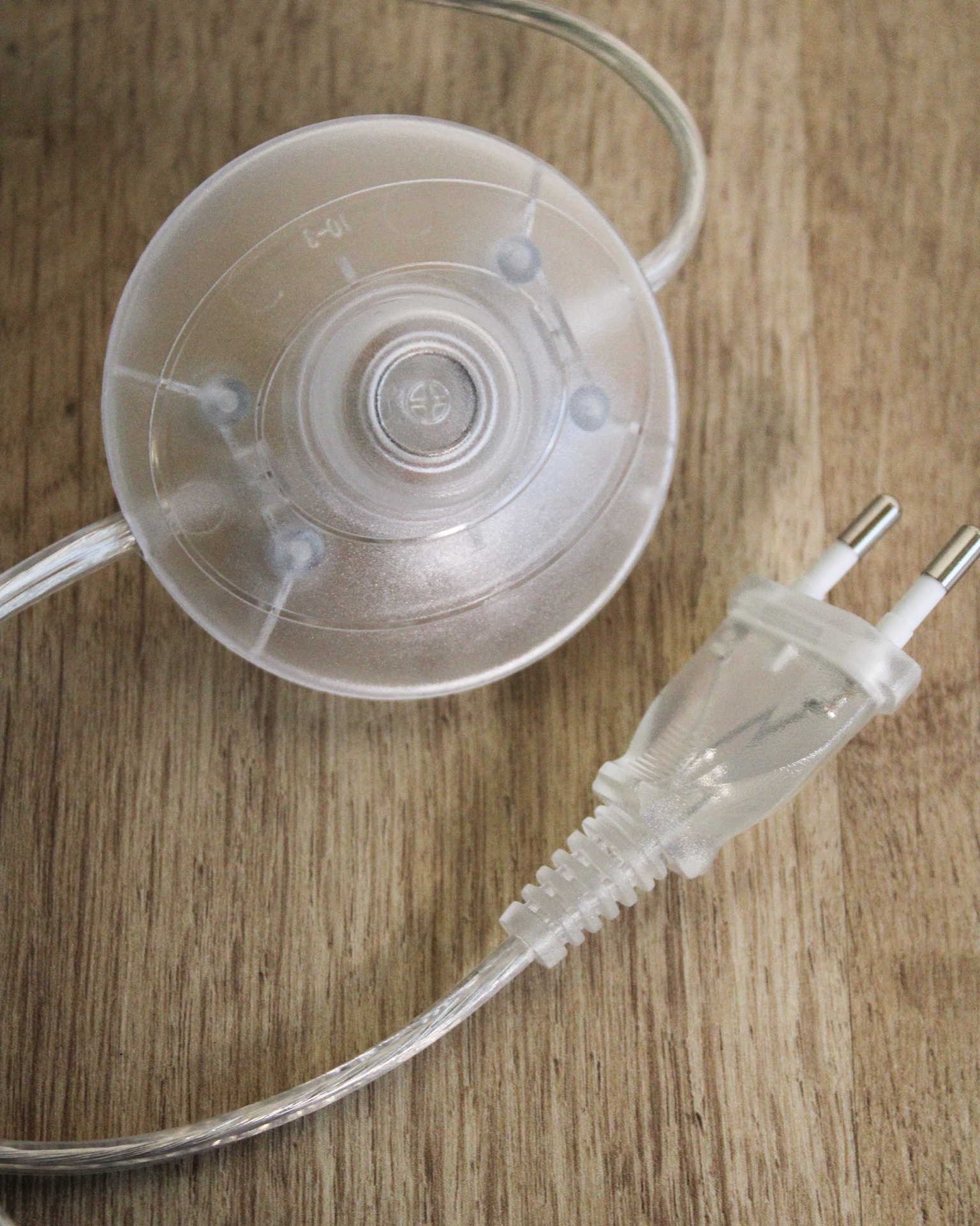 Tomada elétrica de 2 pinos com ventosa transparente e cabo translúcido sobre madeira