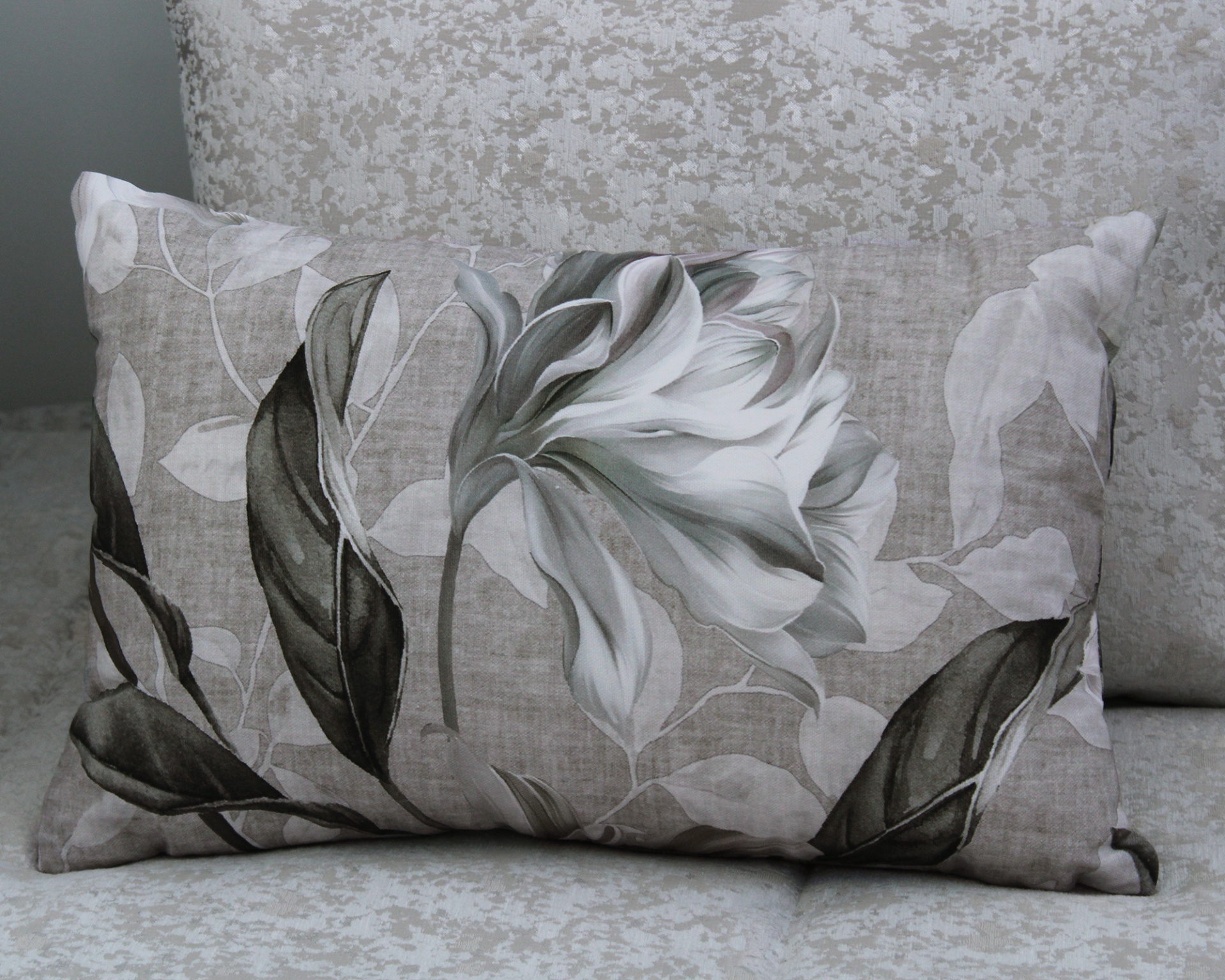 Almofada retangular com padrão floral cinza, branco e preto sobre sofá creme