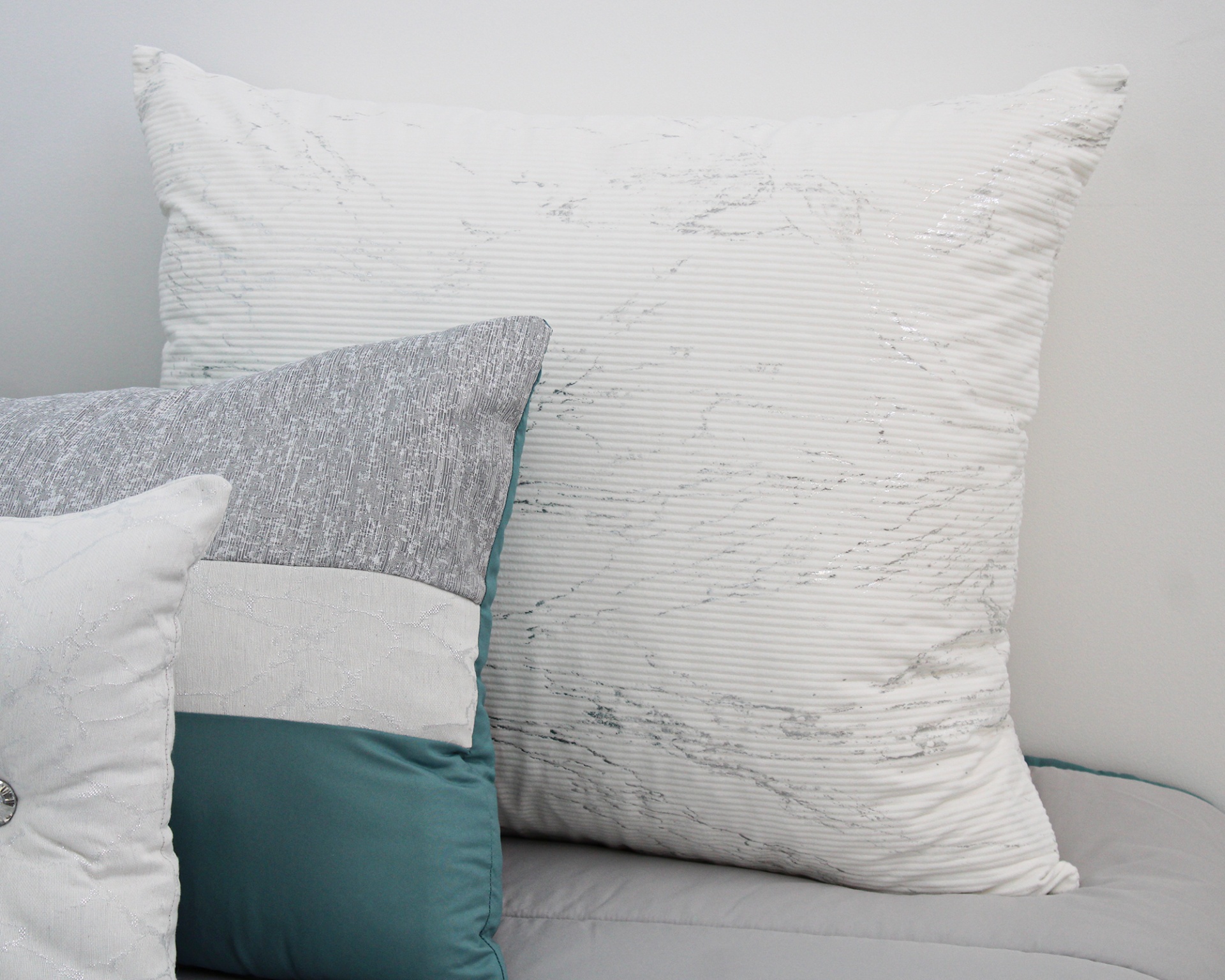 Três almofadas de tecido em diferentes tamanhos e cores sobre superfície cinzenta