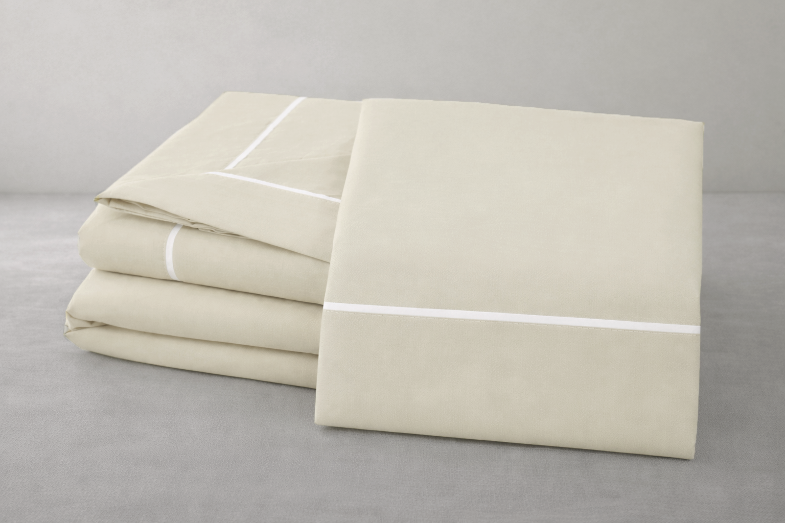 Conjunto de roupa de cama bege claro com linhas brancas finas dobrado sobre superfície cinzenta