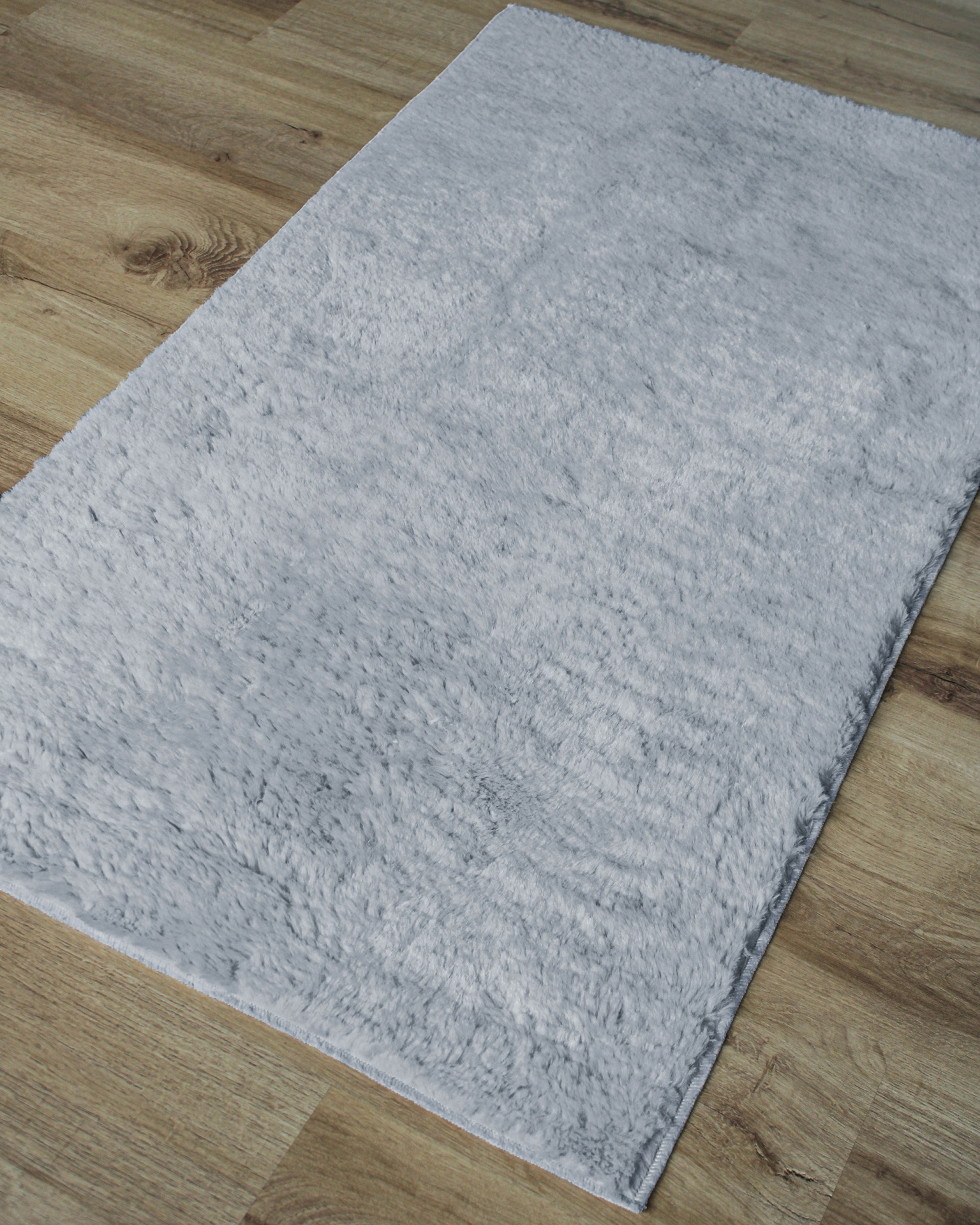 Tapete cinza claro felpudo sobre chão de madeira clara