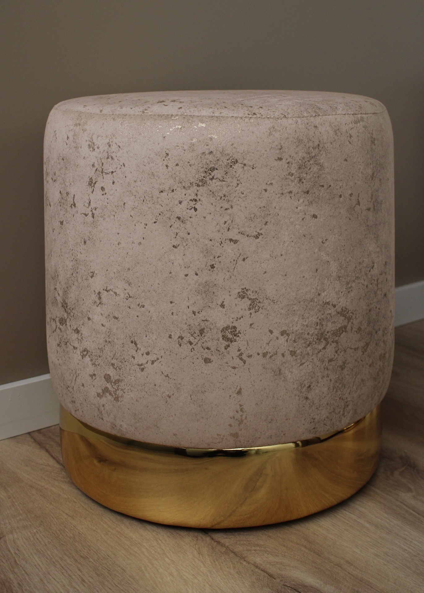 Pufe redondo bege com base dourada em chão de madeira