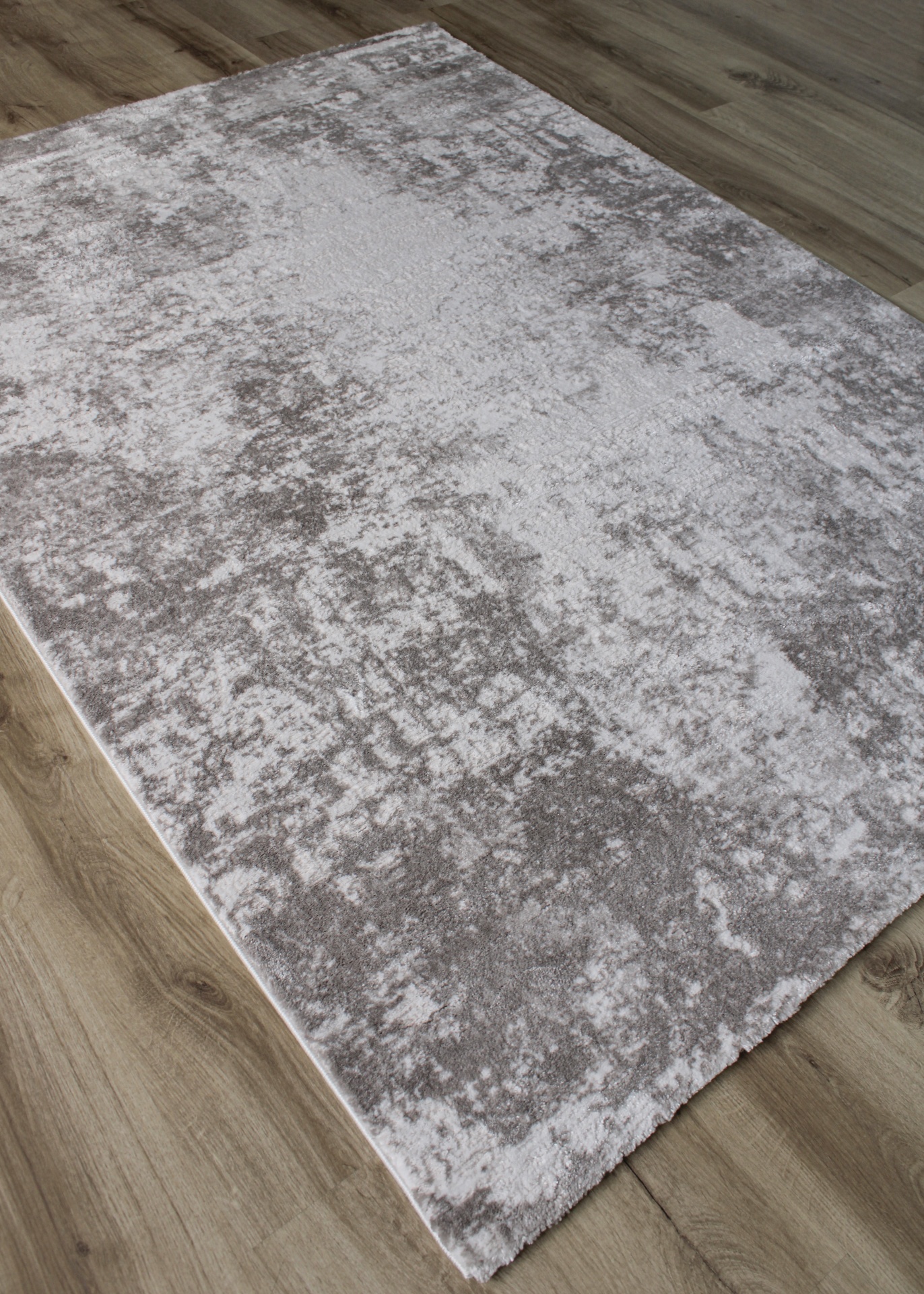 Tapete retangular cinzento claro e branco com padrão abstrato sobre chão de madeira.
