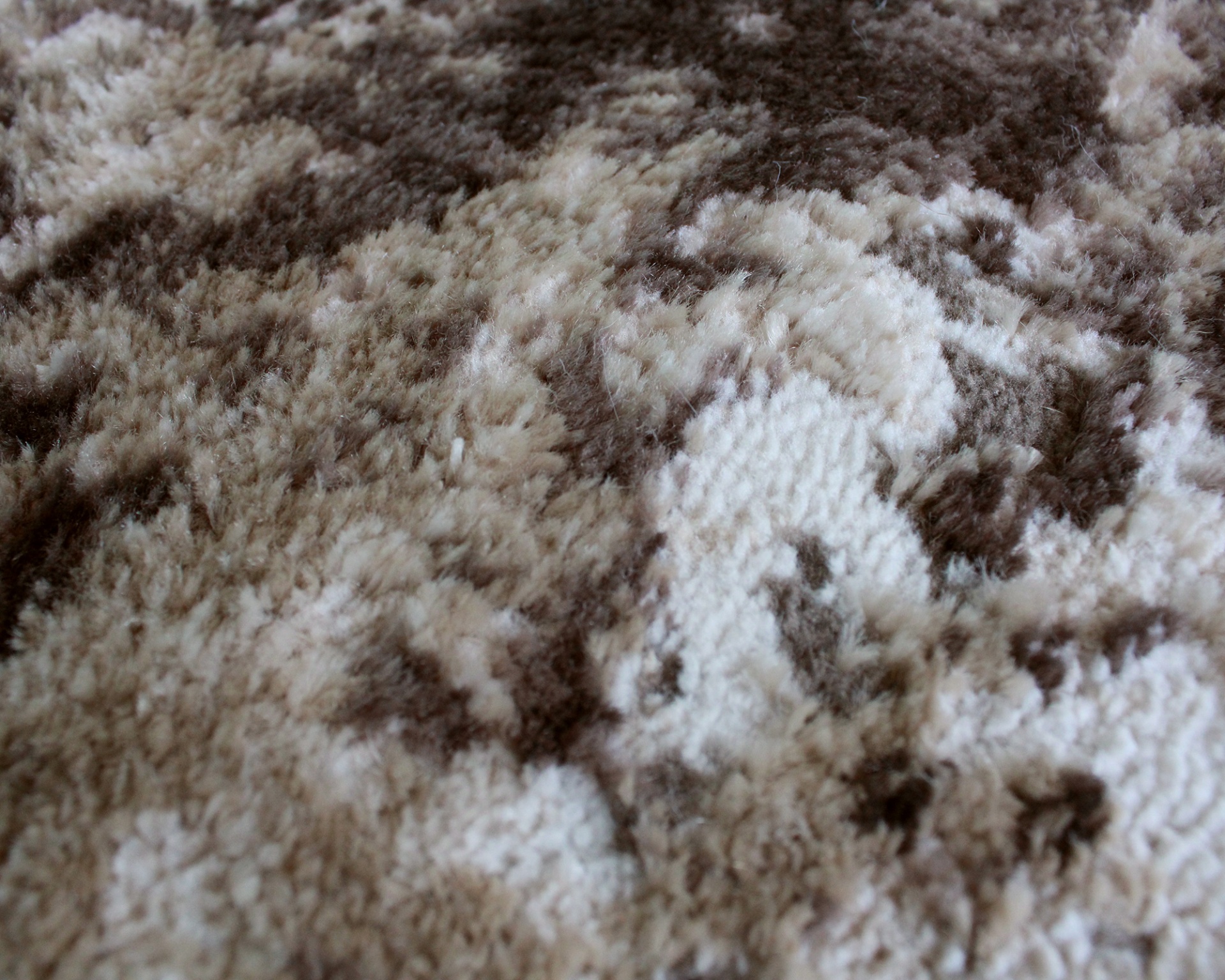 Tapete felpudo com padrão abstrato em tons de bege e castanho.