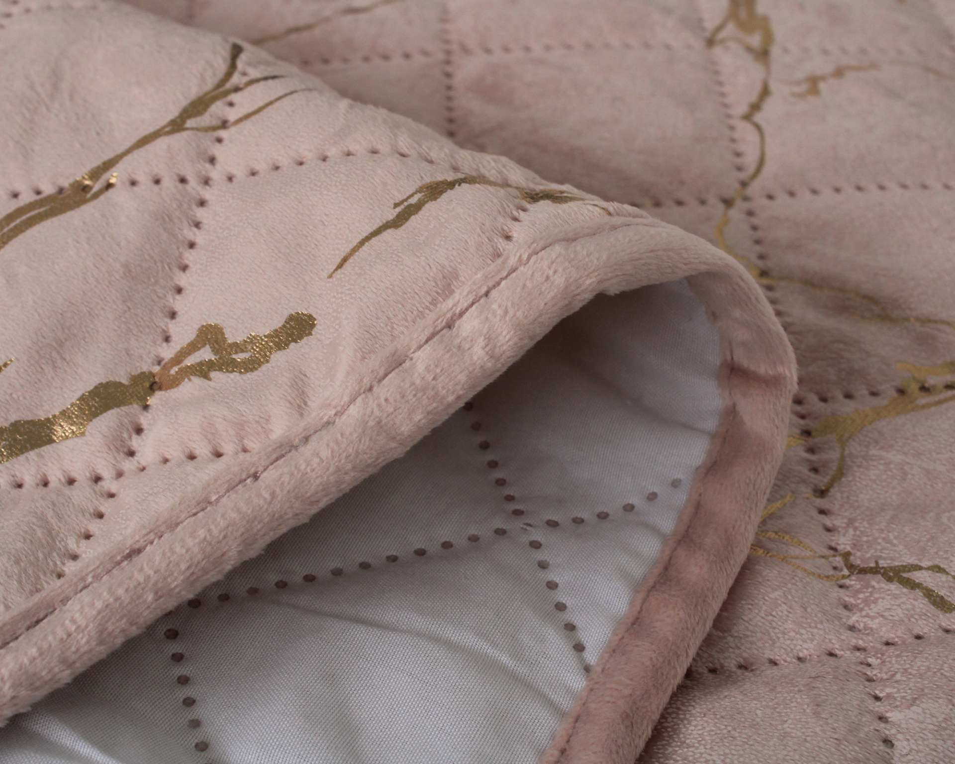 Cobertor ou manta rosa claro com detalhes dourados e costura pontilhada.