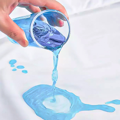 Mão a derramar líquido azul de um copo plástico sobre tecido branco