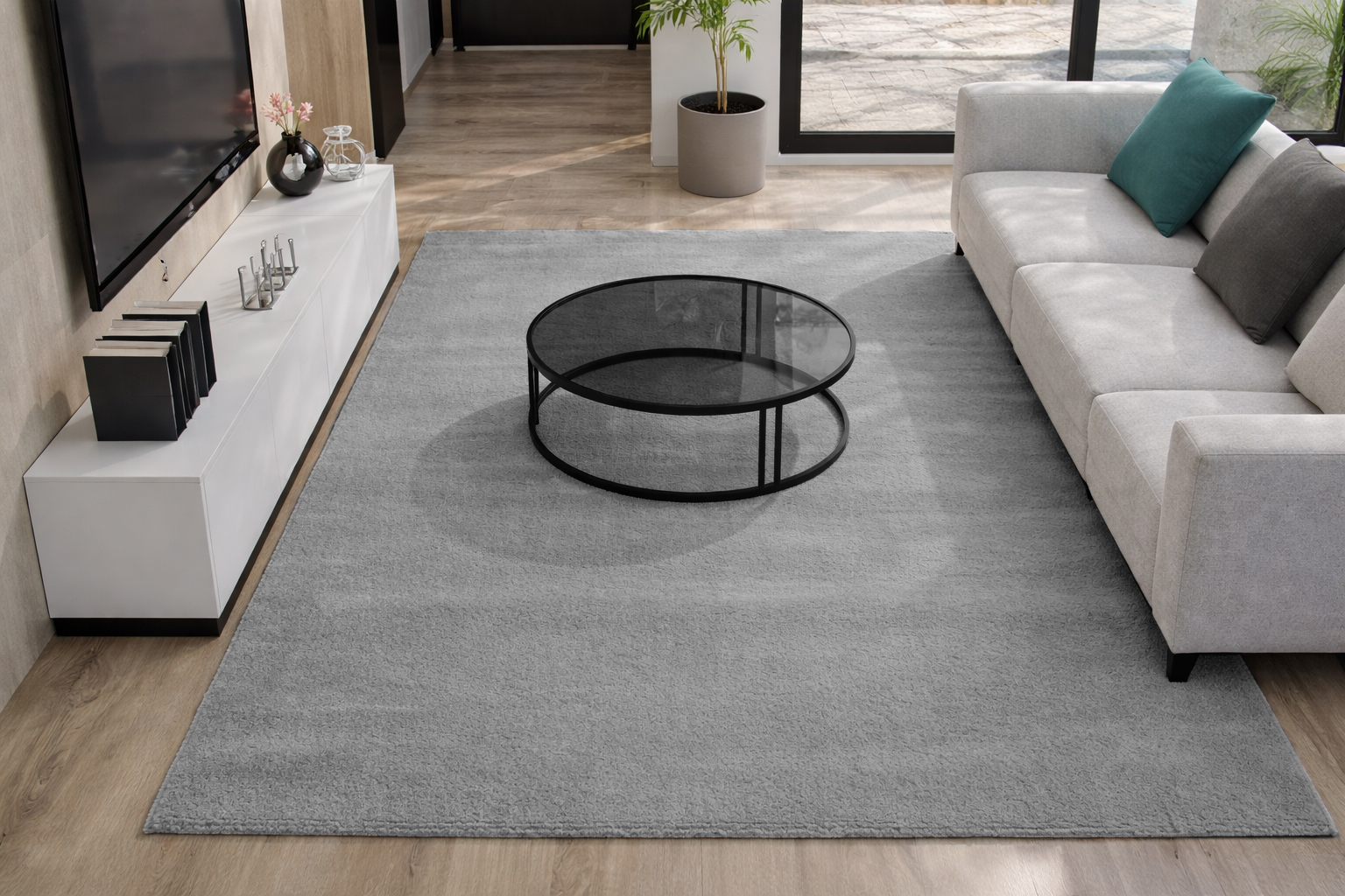 Tapete cinza claro colocado sobre chão de madeira numa sala com mesa de centro redonda de vidro e sofá cinza.