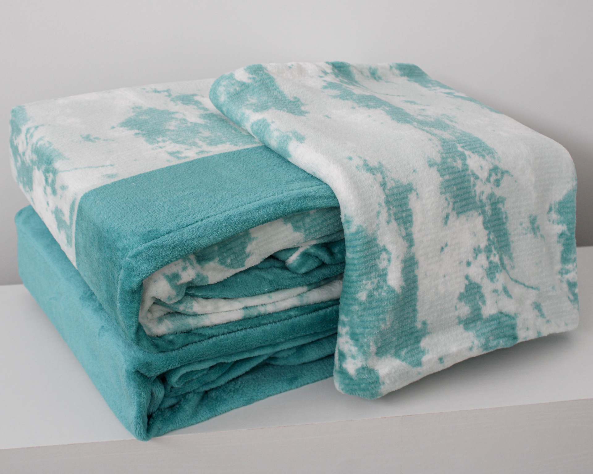 Manta dobrada azul turquesa e branca em superfície branca