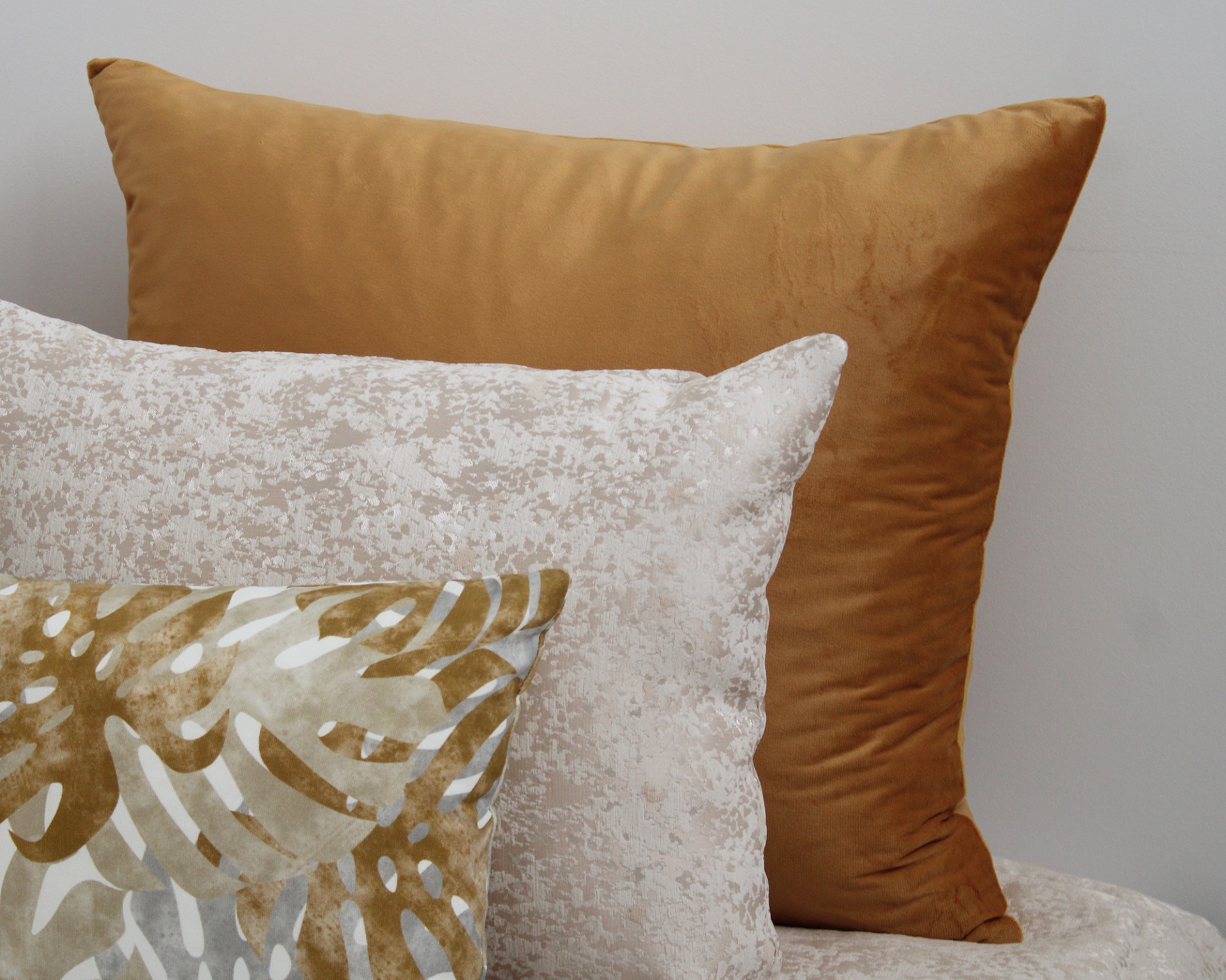 Três almofadas decorativas em tons castanho e bege com texturas e padrão de folhas.