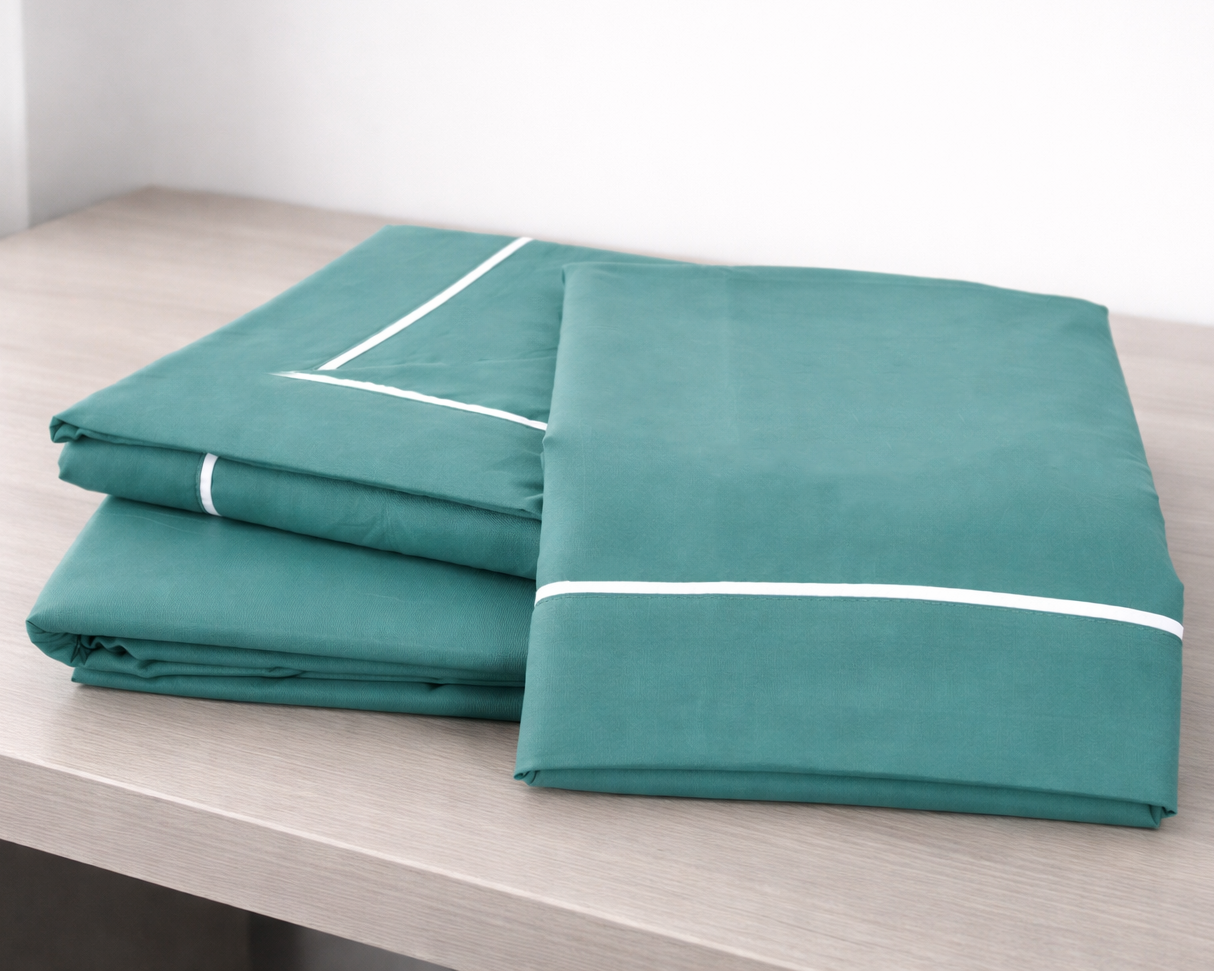 Conjunto de lençóis verdes com fita branca sobre superfície de madeira.