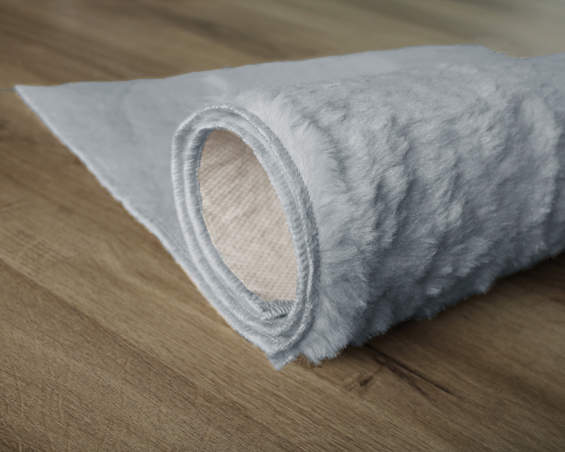Tapete cinza claro felpudo enrolado no chão de madeira