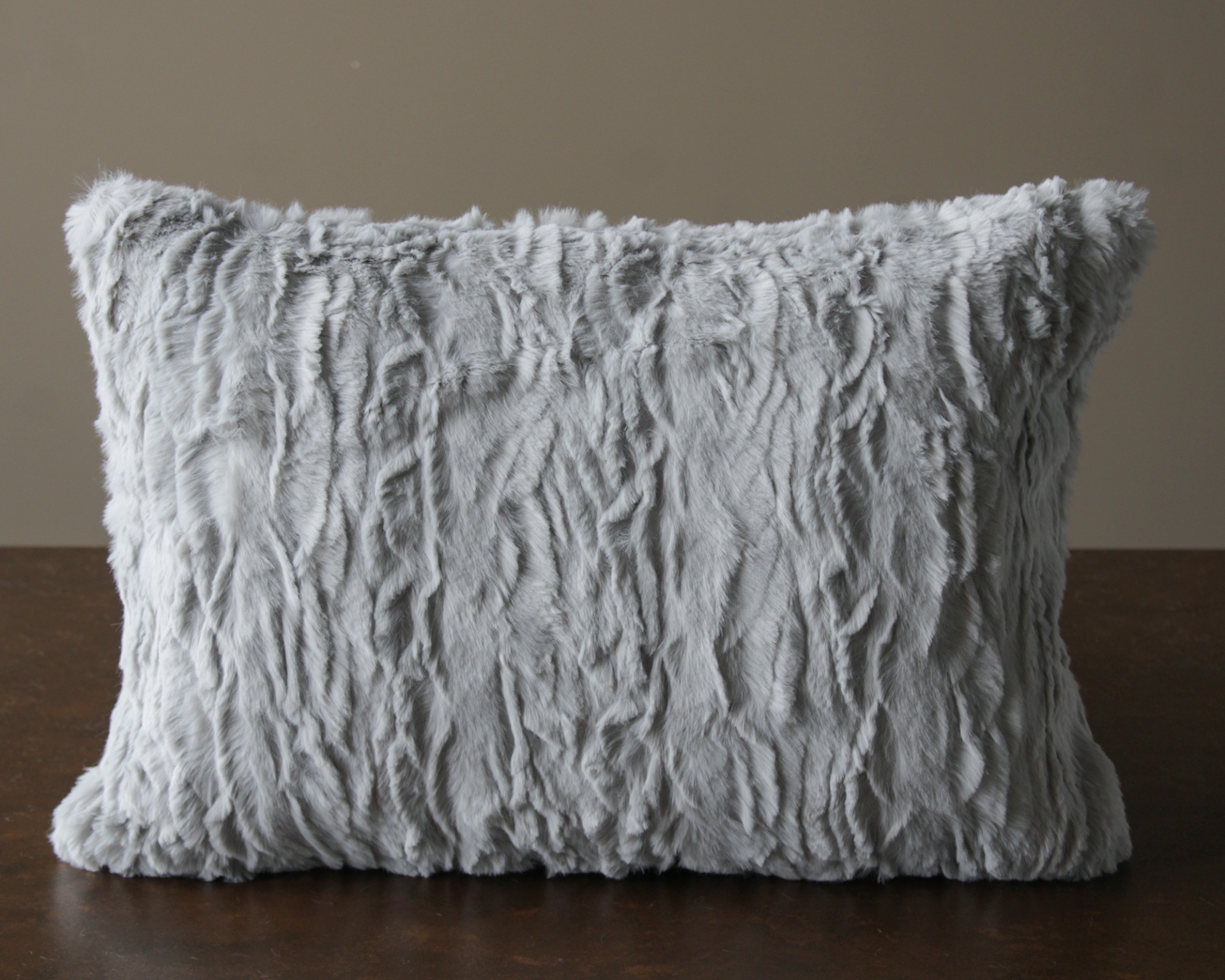 Almofada cinzenta felpuda com textura ondulada sobre superfície de madeira