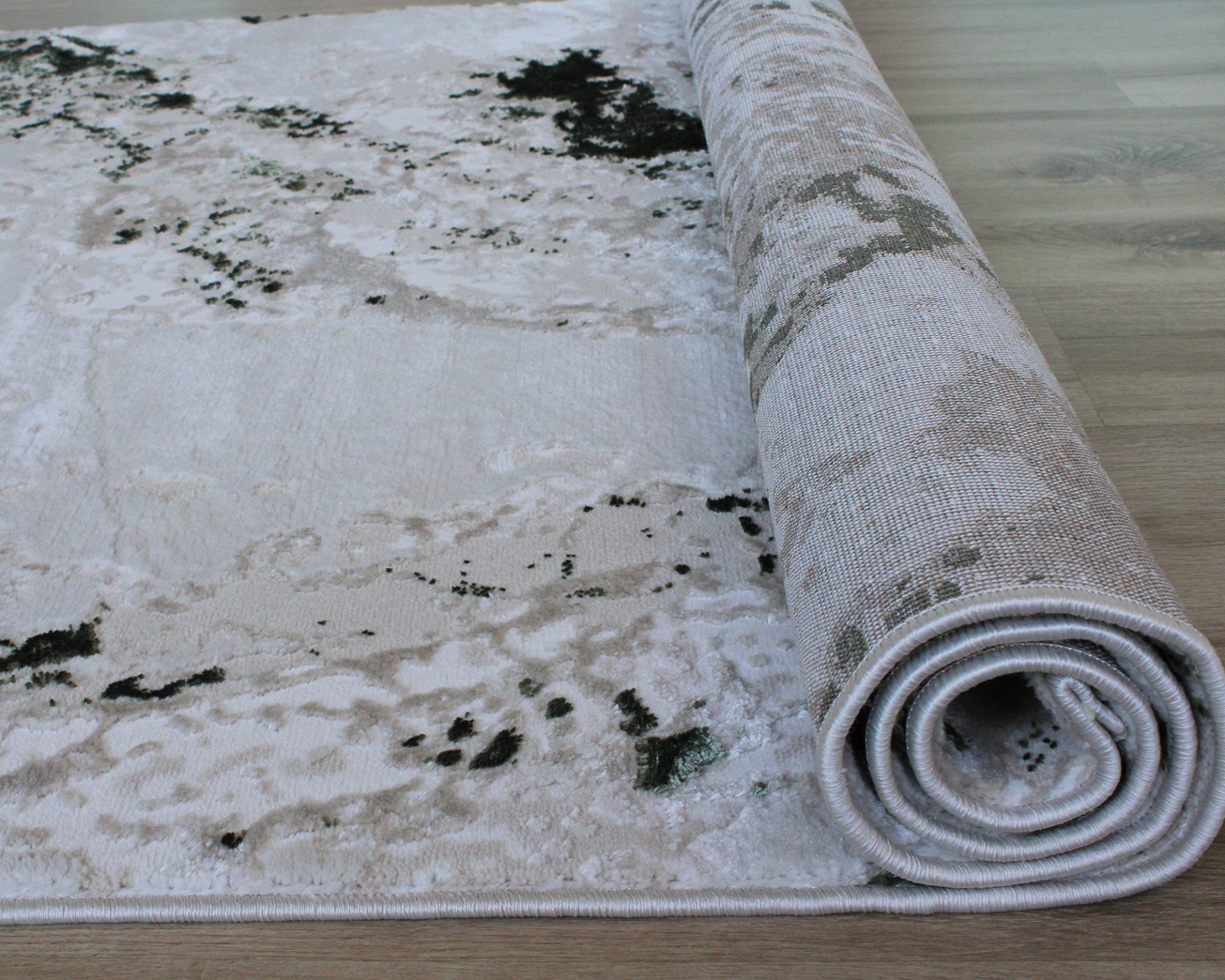 Tapete cinzento claro e bege com padrão abstrato, enrolado numa extremidade, sobre chão em madeira clara.