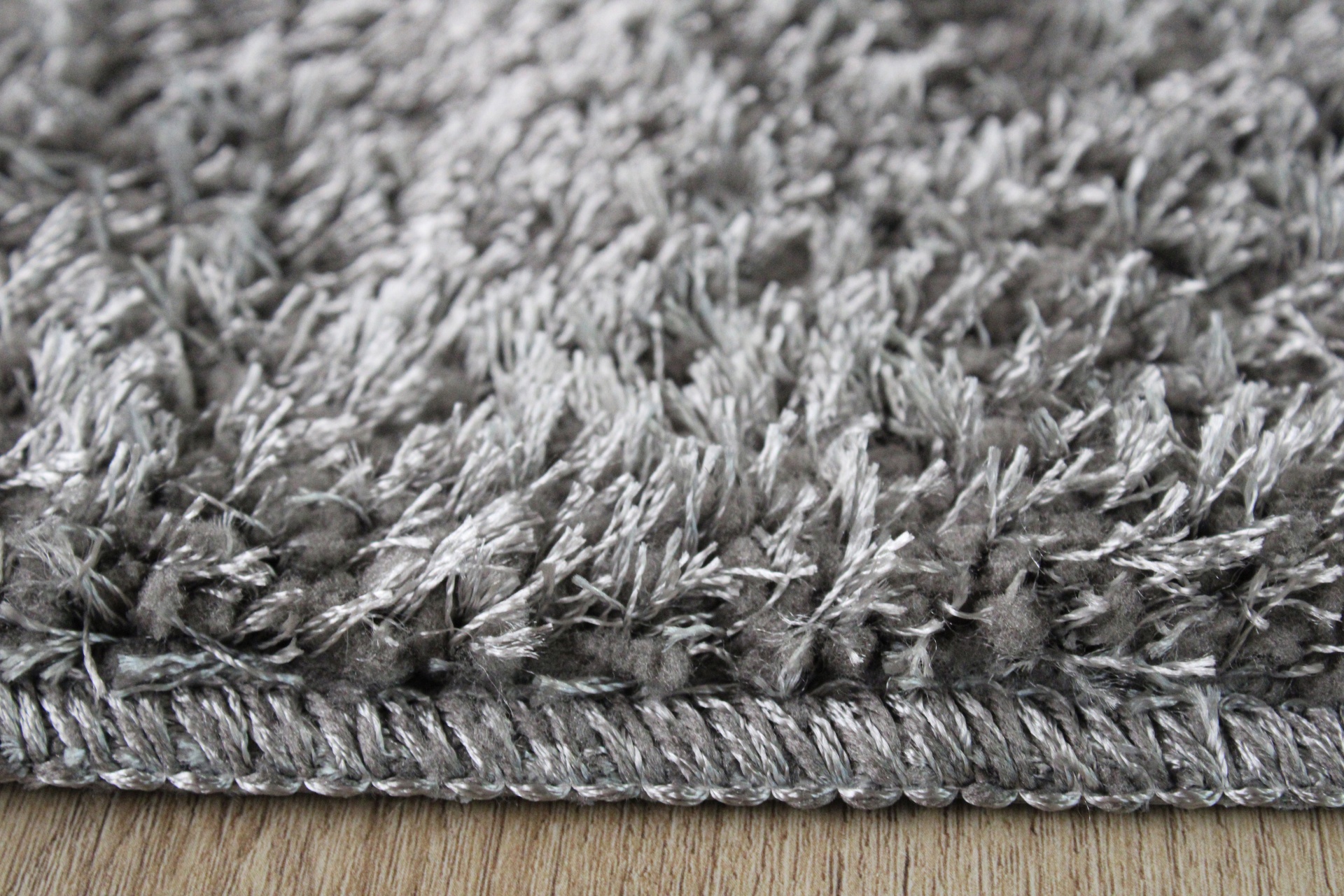 Tapete cinzento de pelo longo com borda bordada sobre chão de madeira