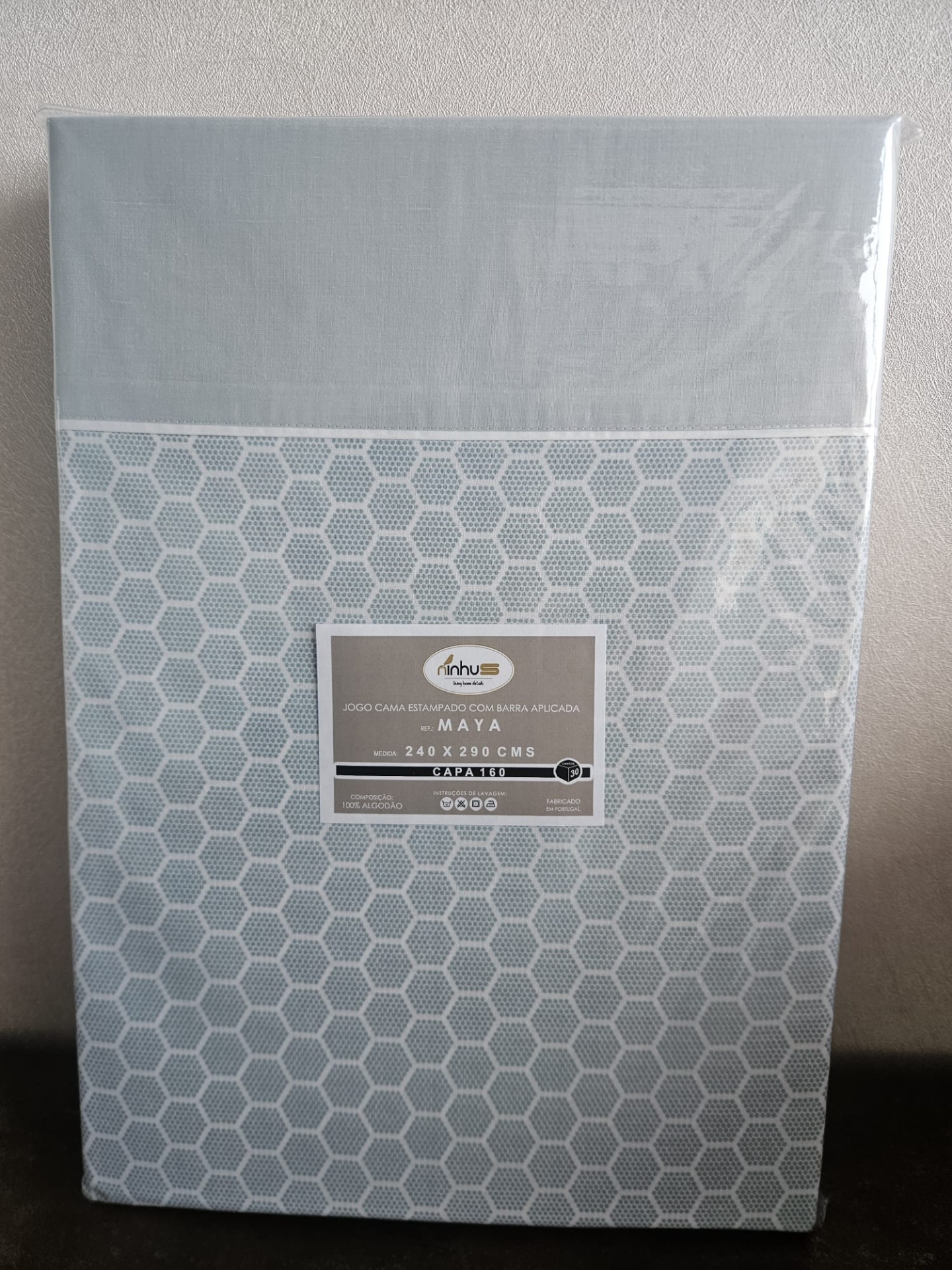 Jogo de cama cinza estampado com padrão hexagonal e etiqueta da marca Minhus