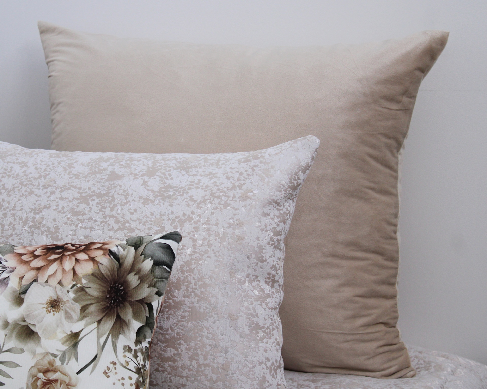 Conjunto de três almofadas decorativas em tons neutros, uma lisa bege, uma texturizada creme e uma com padrão floral.
