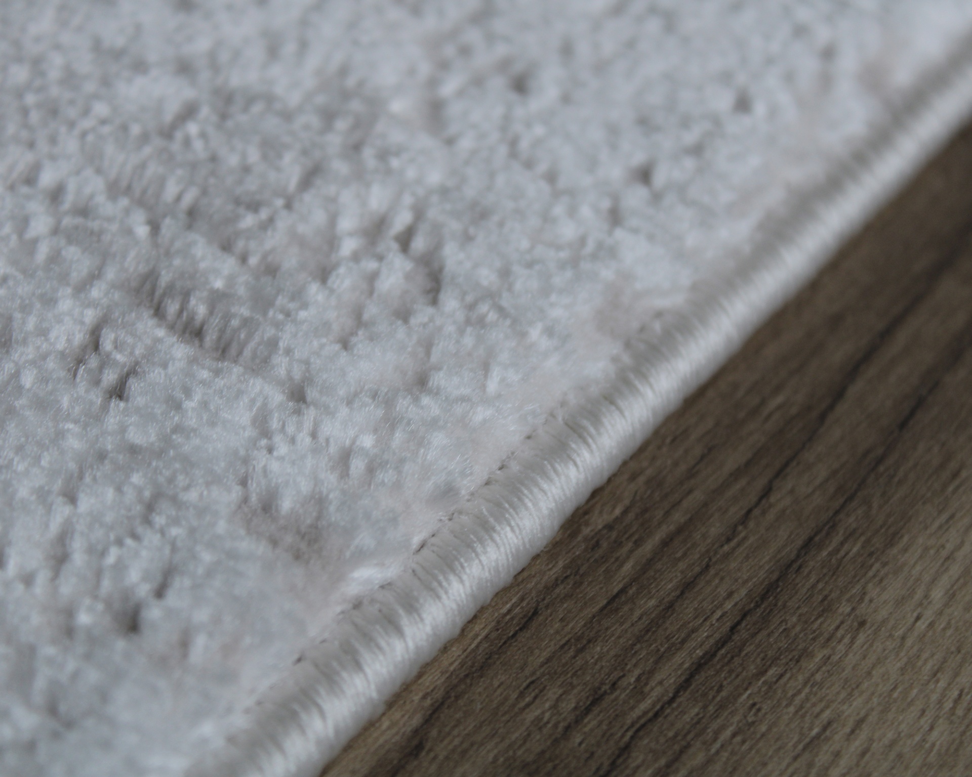 Tapete branco texturizado com borda visível sobre chão de madeira