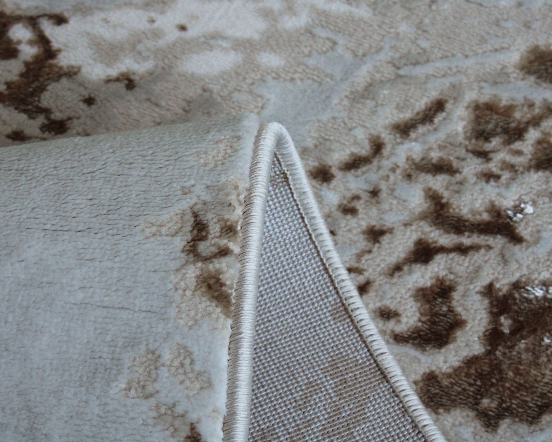 Tapete bege e castanho com padrão abstrato, bordas costuradas e tecido no verso