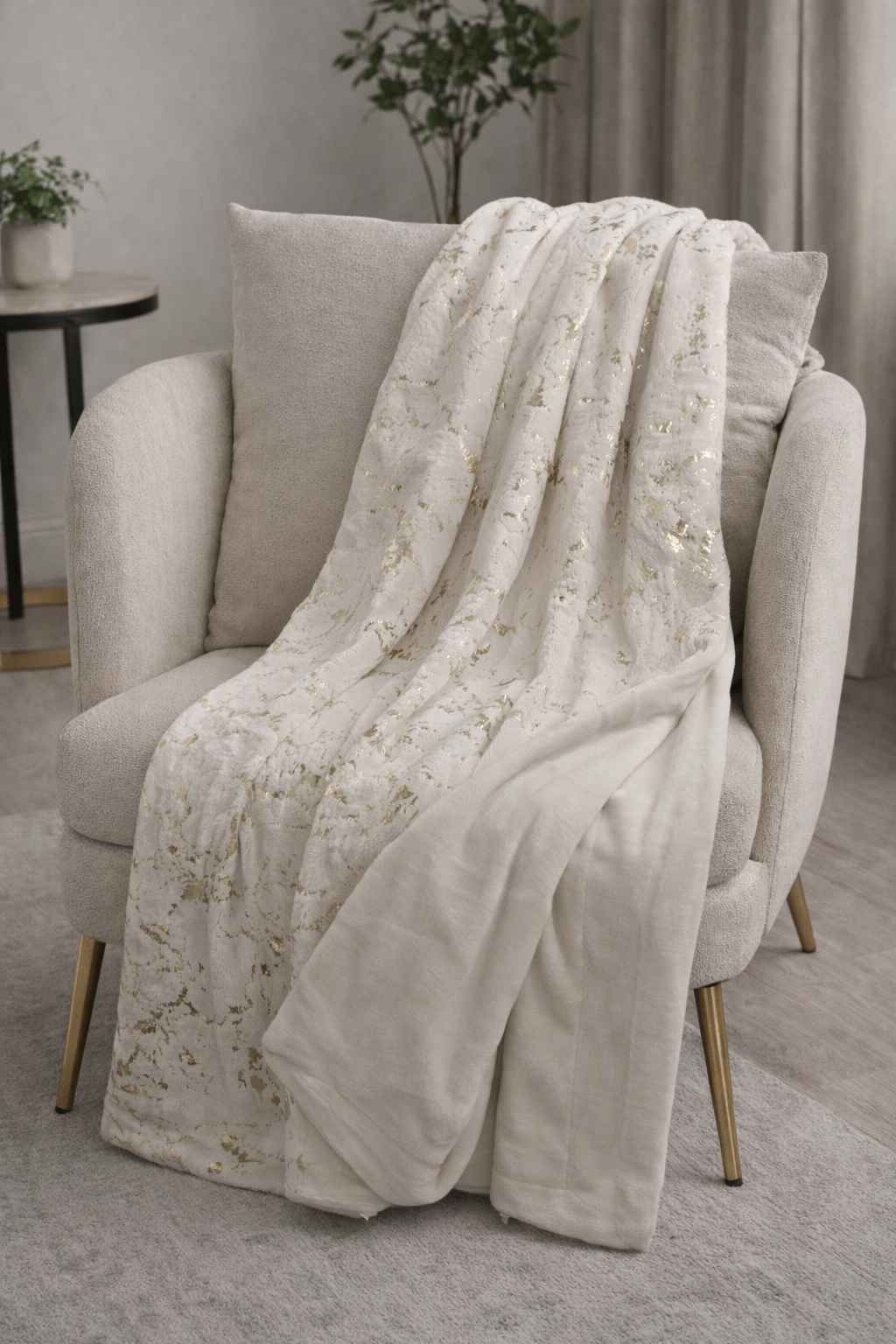 Manta creme com padrão dourado sobre poltrona creme