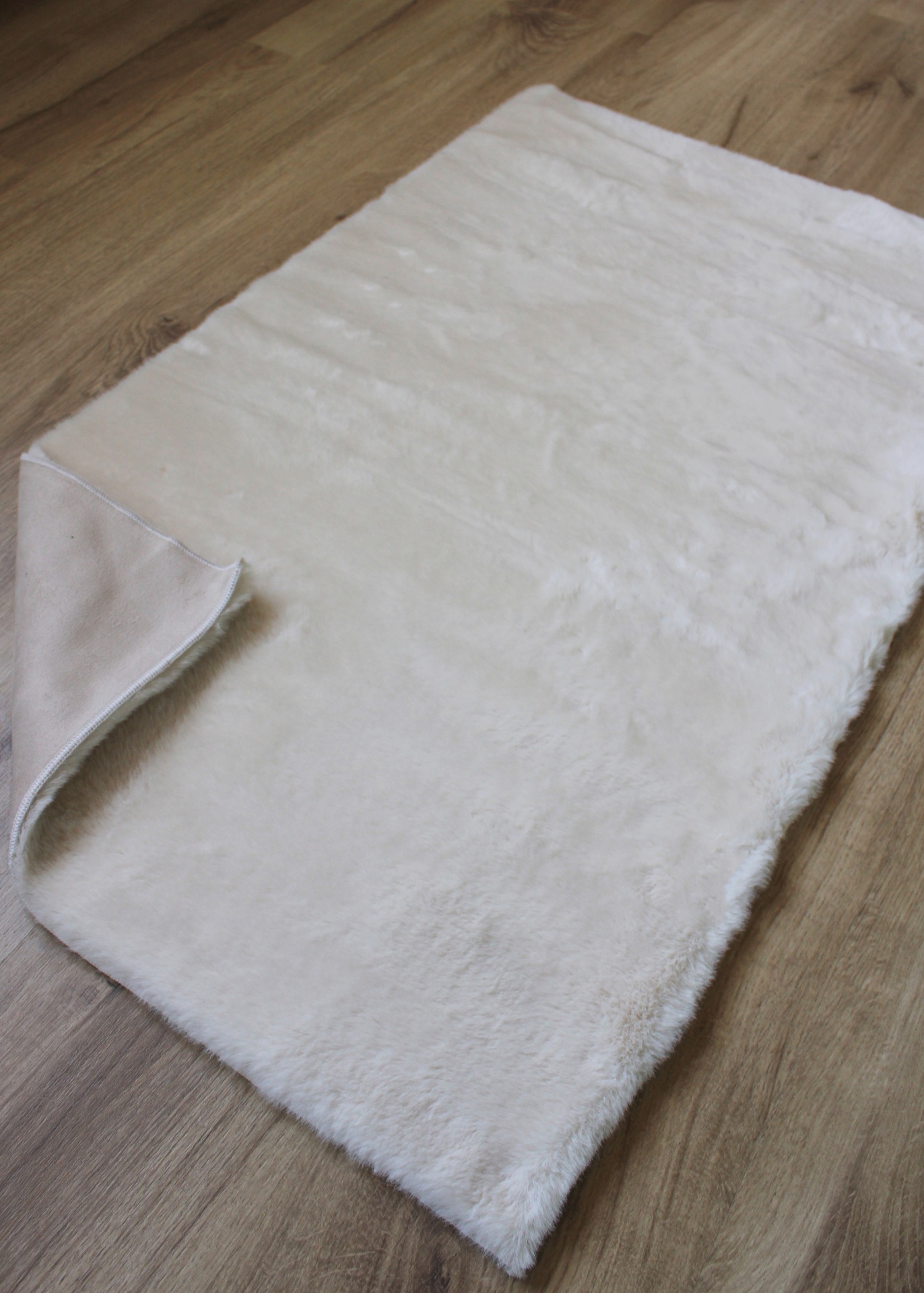 Tapete branco felpudo rectangular sobre piso de madeira clara com canto virado para cima.