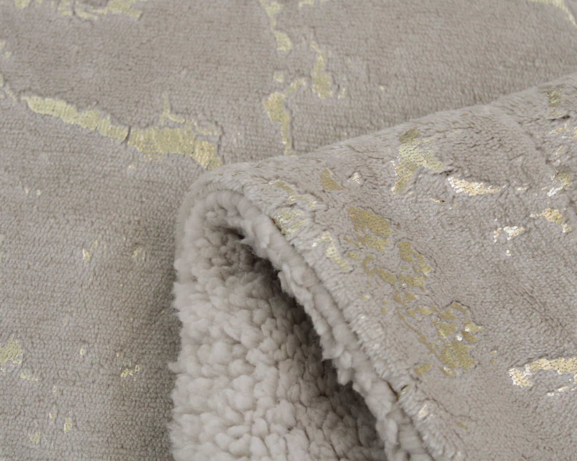 Detalhe de tecido felpudo cinza com padrão dourado metálico e interior aveludado branco dobrado