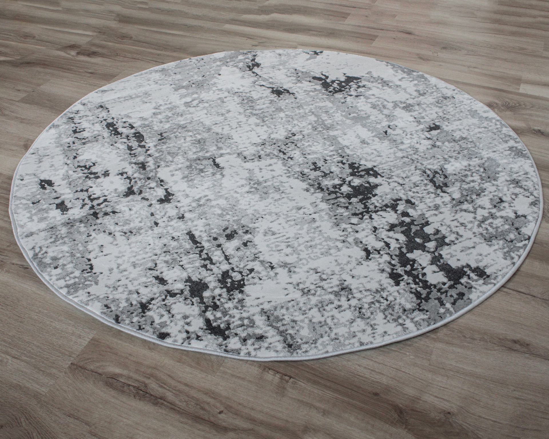 Tapete redondo cinza e branco sobre chão de madeira clara